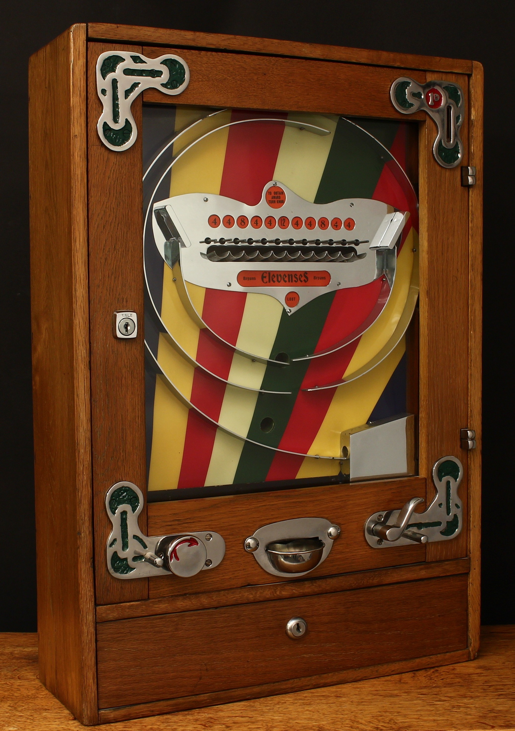 A 1950's Bryans (Bryans Works, Kegworth, Derby) Elevenses 'Allwins' mechanical penny slot arcade/amusement machine with manual payout, rounded rectangular shaped oak case, the inner multicoloured back plate with a single line of eleven cups, curved trigger, glazed hinged door, 64cm high, 44.5cm wide, 15cm deep