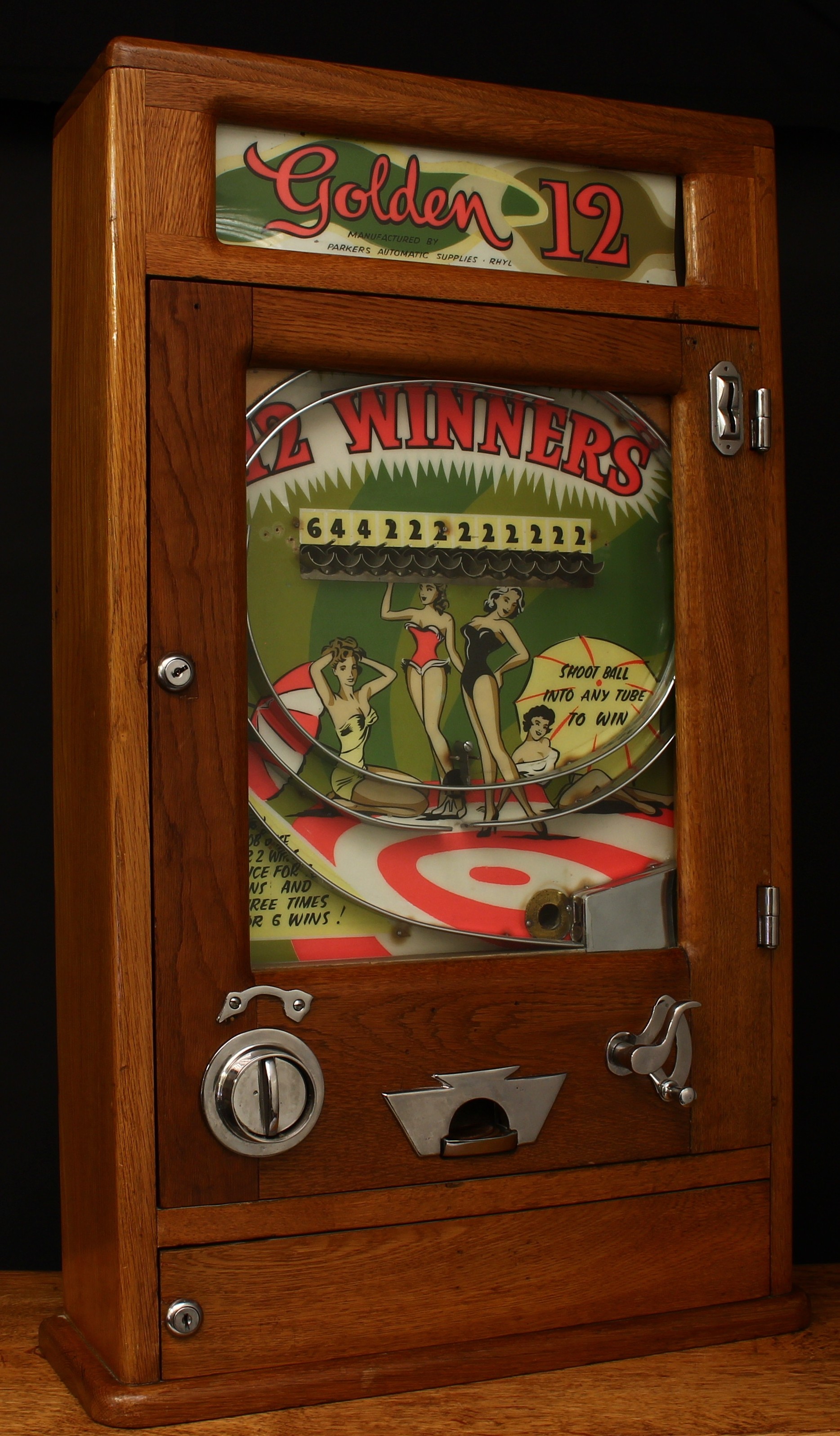 A Parkers Automatic Supplies (Rhyl, Wales) Golden 12 mechanical penny slot arcade/amusement machine with manual payout, rounded rectangular shaped oak case, the inner pictorial back plate illustrated with bathing Belle, single line of twelve cups, curved trigger, glazed hinged door, 81cm high, 46cm wide, 15cm deep