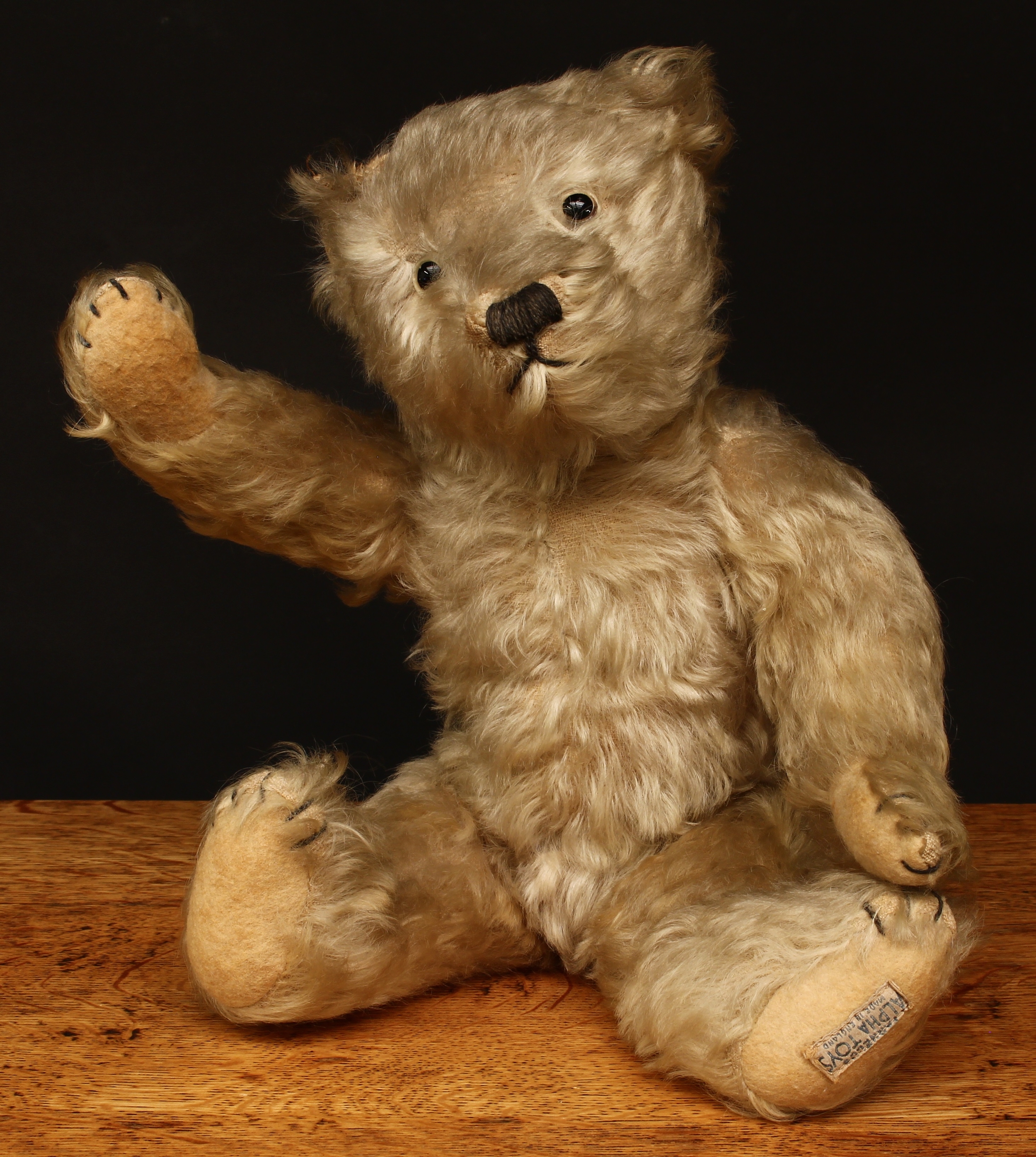 A 1930's J.K.Farnell (John Kirby Farnell) golden mohair jointed teddy bear, clear and black glass eyes, pronounced snout with brown vertically stitched nose and mouth, cream felt pads to hands and feet with brown stitching, trademark blue and white rectangular shaped label to foot 'FARNELL'S ALPHA TOYS, MADE IN ENGLAND', 36cm high