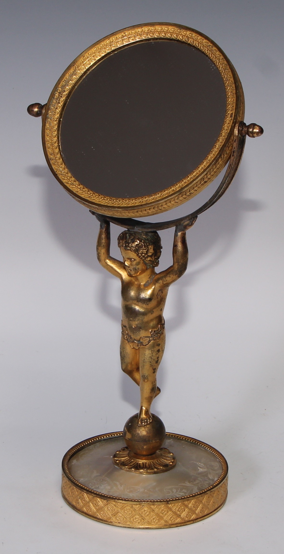 A French Palais Royale gilt bronze and mother of pearl table mirror, the circular tilting plate supported by a scantily clad putto, engraved base, 29cm high, c.1870