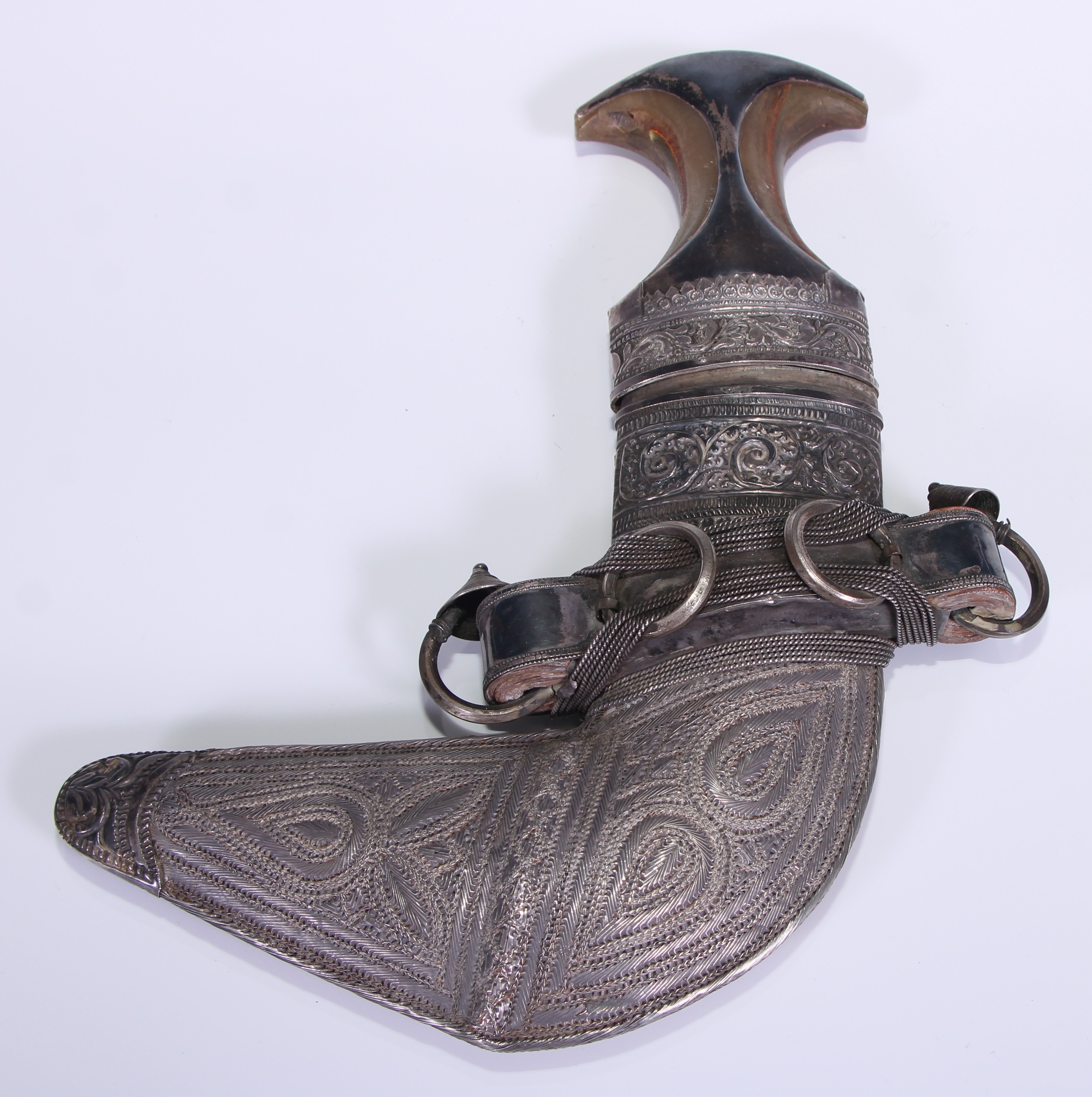 A Middle Eastern silver mounted jambiya dagger, 17cm curved blade with central ridge, horn grip, the scabbard chased with leafy scrolls and stylised wirework lotus, 30cm long