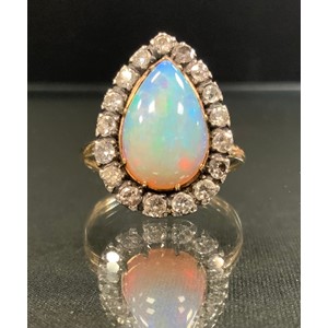 An opal and diamond ring, large pear cabochon opal, flashing vibrant green, blue and violet colour play, measuring approx 15mm x 9.5mm, surrounded by seventeen old brilliant cut diamonds, total estimated diamond weight approx 1,0ct, unmarked gold coloured metal shank, size R, 4.6g gross