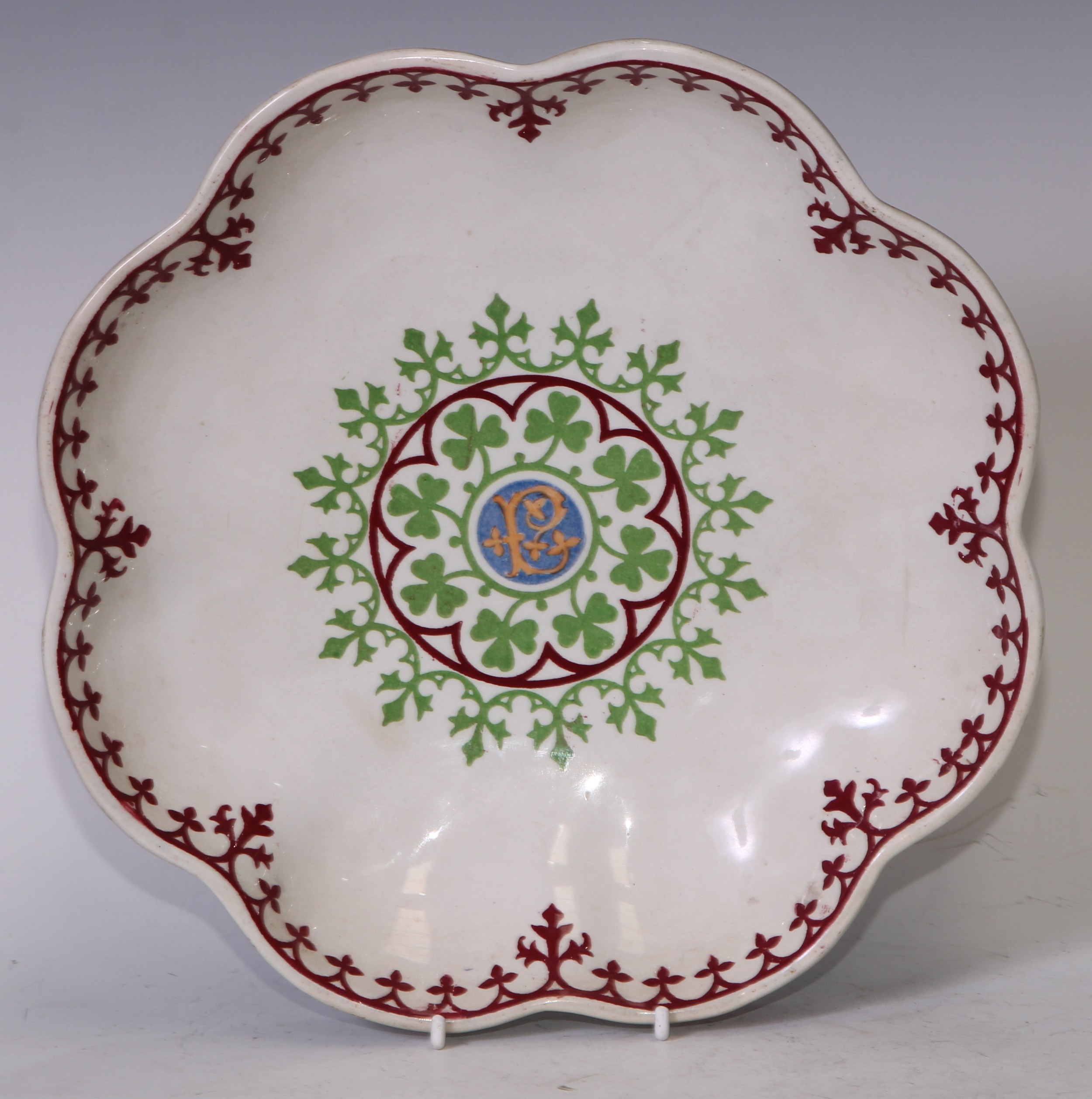 Augustus Welby Northmore Pugin (1812–1852) - a Minton and Hollins New Stone shaped circular dish, designed by Pugin for the Palace of Westminster, with central Gothic P within a clover leaf roundel, the rim in iron red with Gothic tendrils, 26.5cm wide, impressed marks  The remaining service is stored at the Palace of Westminster, but not on public display. There are almost 200 pieces which were acquired in 1983 after being discovered in the Priest’s House, St Mary’s Roman Catholic Church, East Hendred by Reverend Anthony Fagan.  The service was originally used by Pugin and his family in their home, The Grange, in Ramsgate.  These are two three plates know to exist outside he Palace of Westminster