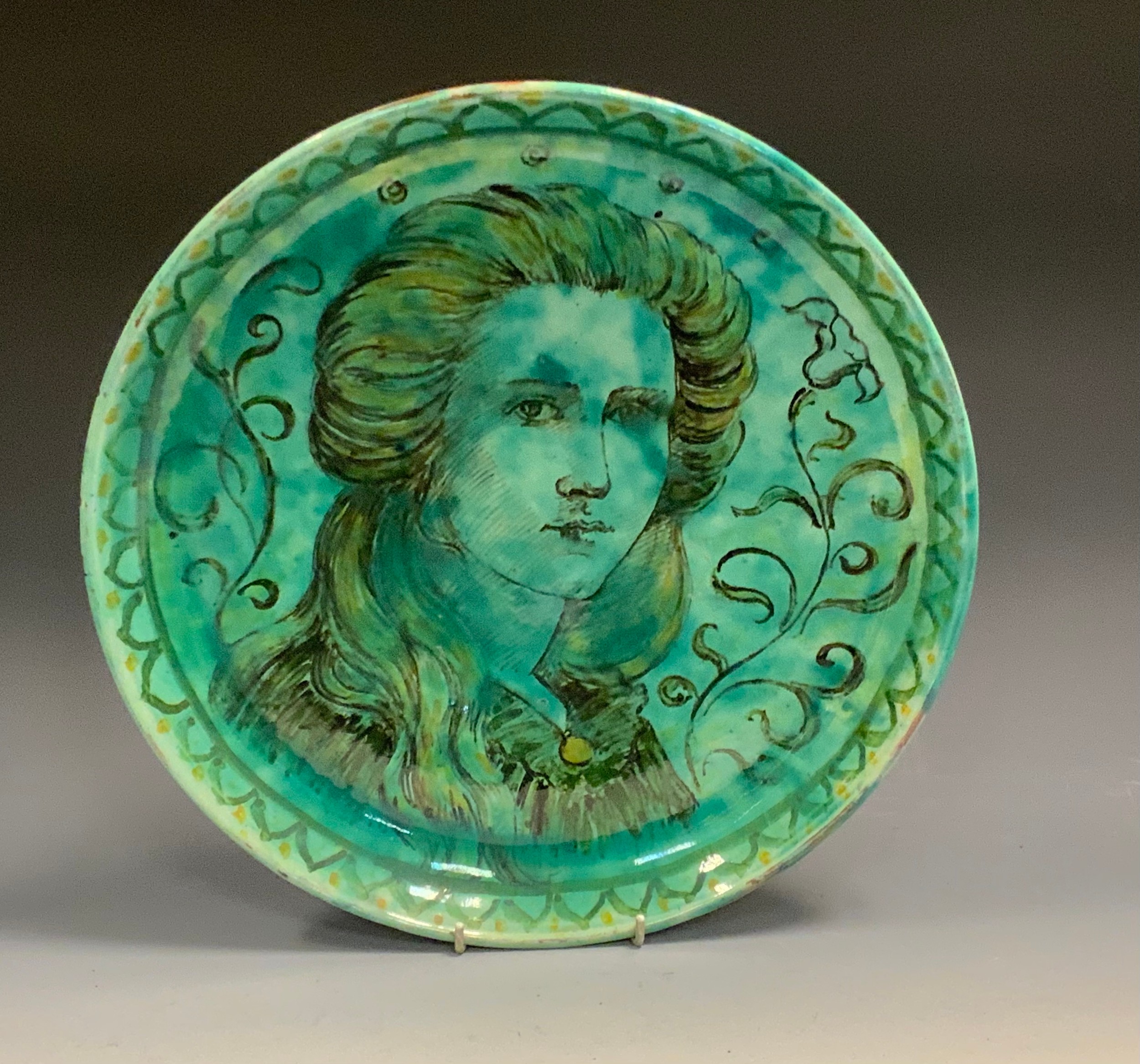 A Della Robbia charger, painted by Harold Rathbone, with a portrait of Enid Woodhouse, in black, picked out in yellow in a mottled sea green ground, 35cm diam, painted mark, inscribed My Enid Woodhouse, by H Rathbones 1896