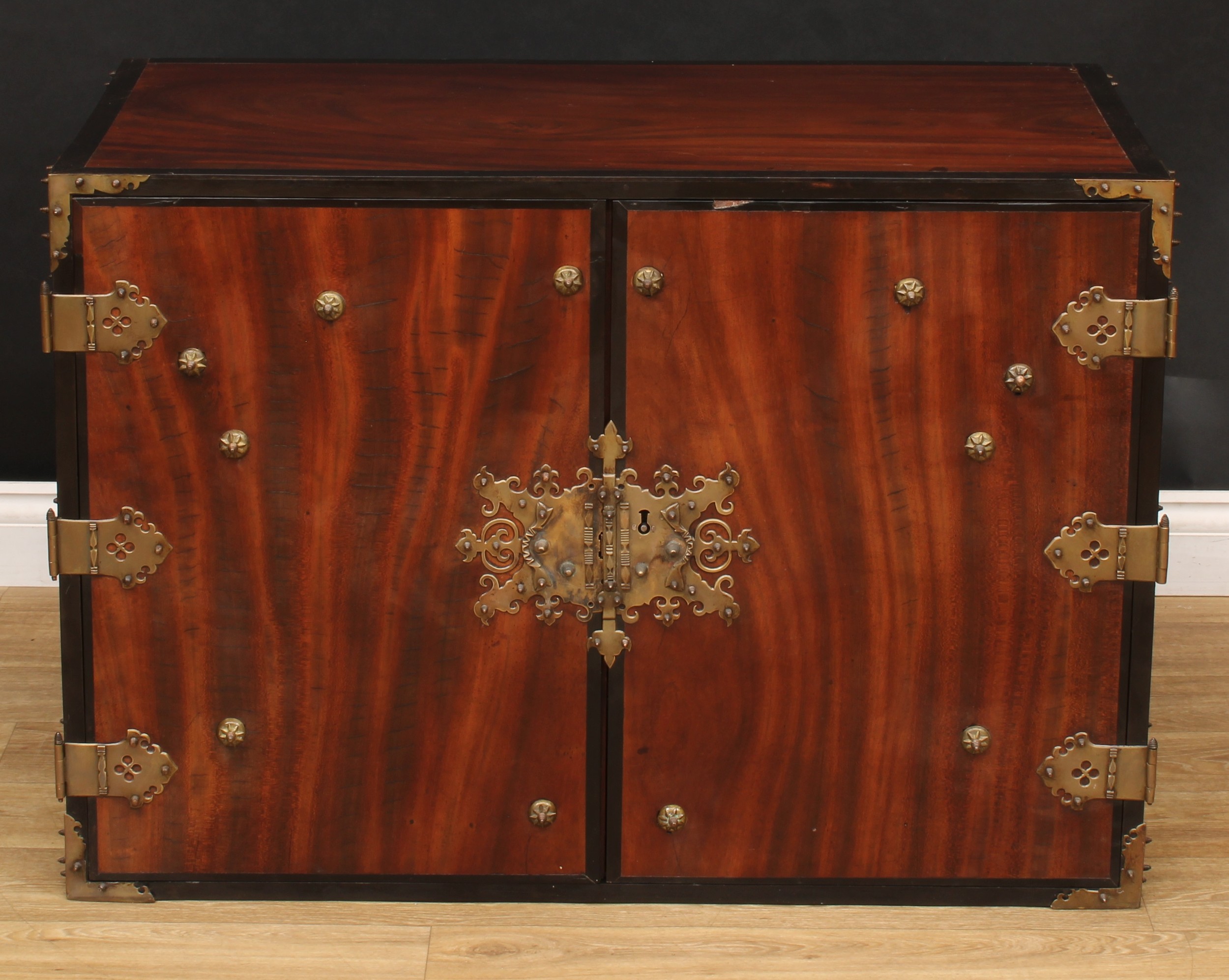 A 19th century colonial brass mounted ebony banded hardwood enclosed chest, possibly Batavian, the pair of panel doors enclosing an arrangement of four short and two long drawers, applied throughout with pierced brass mounts, 66.5cm high, 95.5cm wide, 52.5cm deep
