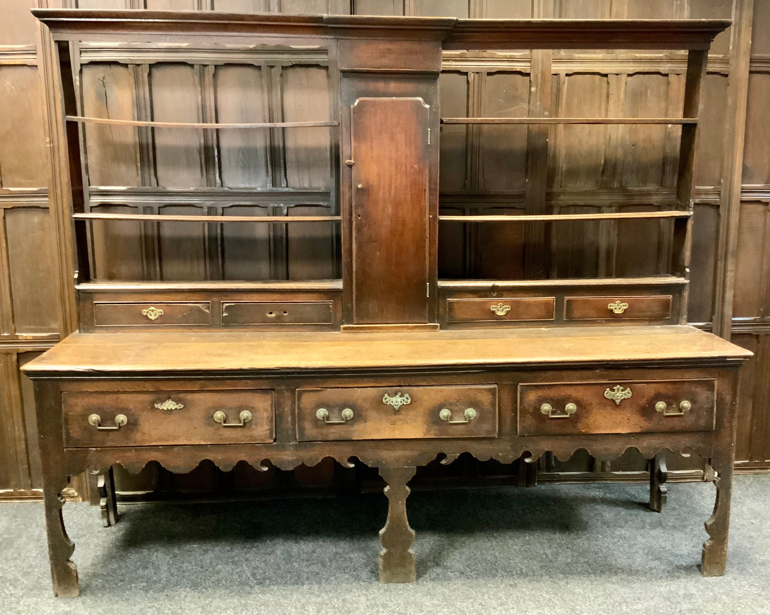 An 18th century oak dresser, c.1760  moulded cornice above open shelves with central cupboard door above four short drawers, the projecting base with three drawers, shaped apron and fore legs  198cm high 232cm wide 60cm deep