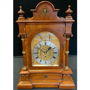 A Victorian oak bracket musical clock, 18.5cm dial with silvered chapter ring, Roman numerals,  Eight Bells and Cambridge Chimes subsidiary dials, the gilt ground applied with leafy scrolls, the double fusee movement signed John Moore, Clerkwell Close, London. three winding holes, eight day movement, striking on gongs, the case with shaped arched pediment centred with gilt mask, turned finials, the glazed arched door flanked by Corinthian columns, breakfront base carved with gilt chevrons, 63cm high, 43cm wide, c.1870