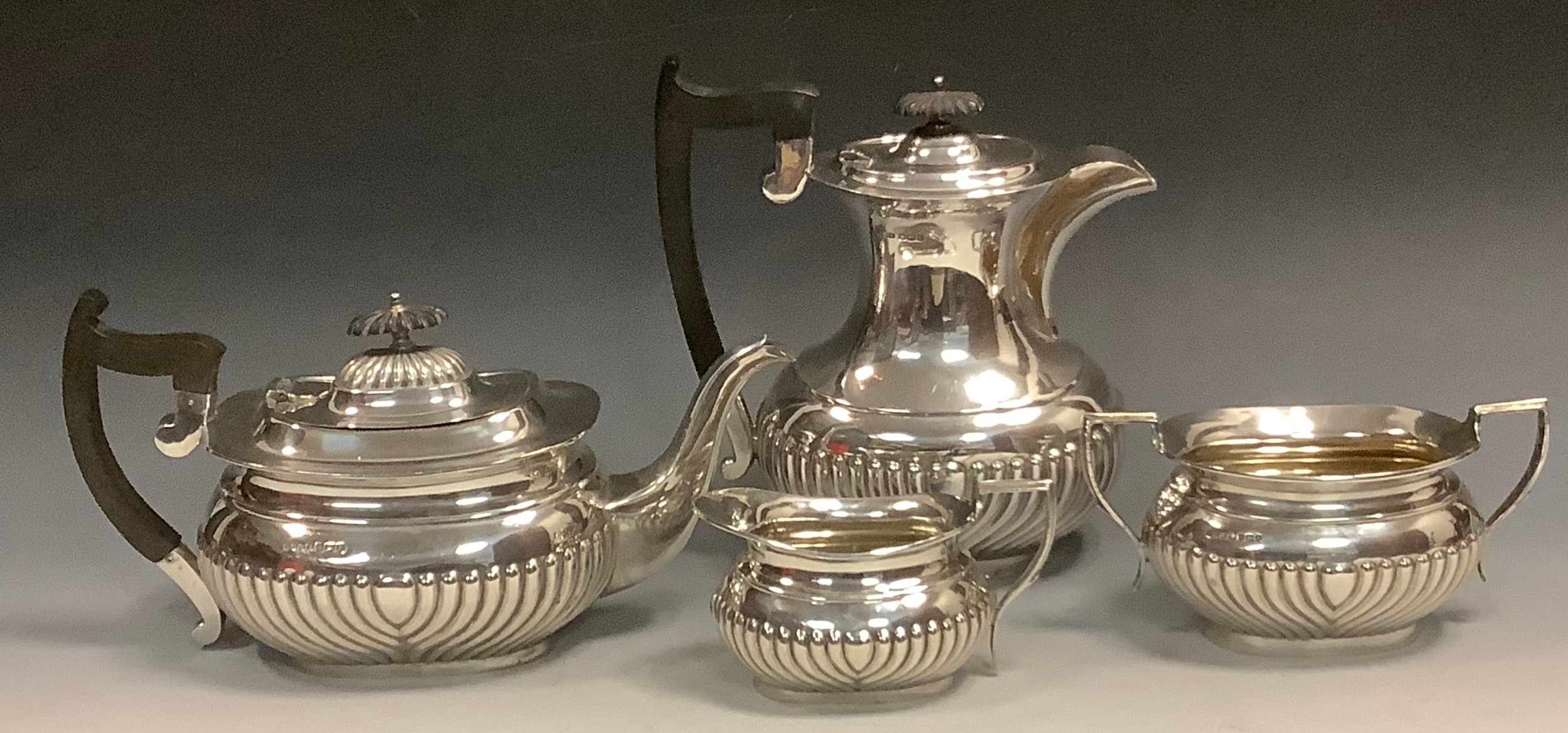 A silver half fluted boat shaped three piece tea service, comprising teapot,  milk jug and sugar bowl, ebonised finials and handles, Viner's Ltd, Sheffield 1910 and 1911;  a similar hotwater jug, 23c.m high, Sheffield 1922, 67ozt