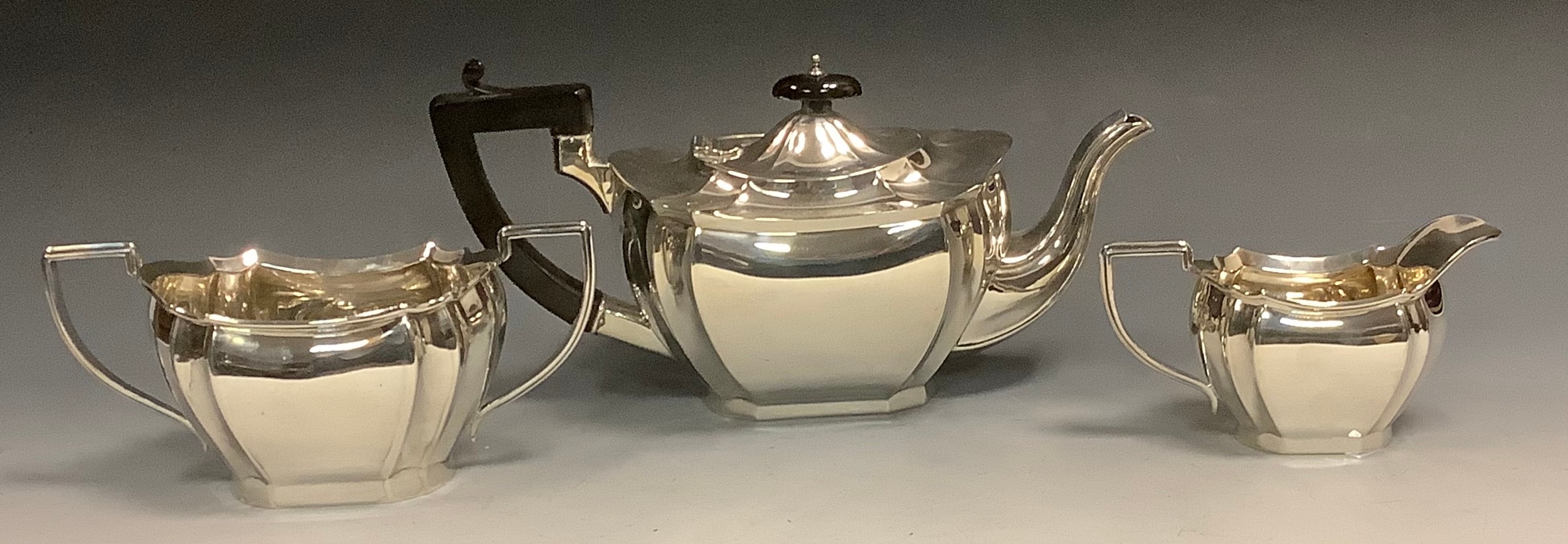 A silver three piece panelled boat shaped tea service, ebonised button final, angular handle, William Aitken, Birmingham 1927, 40ozt