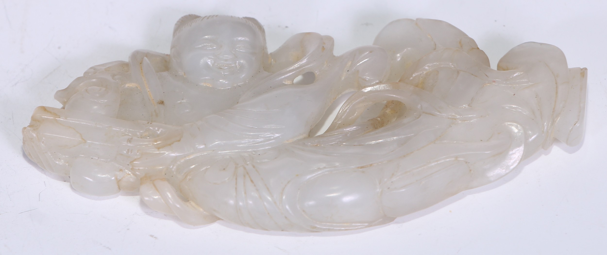 A Chinese pale nephrite plaque carved with a boy holding a box, late Qing dynasty, 8.5cm wide.