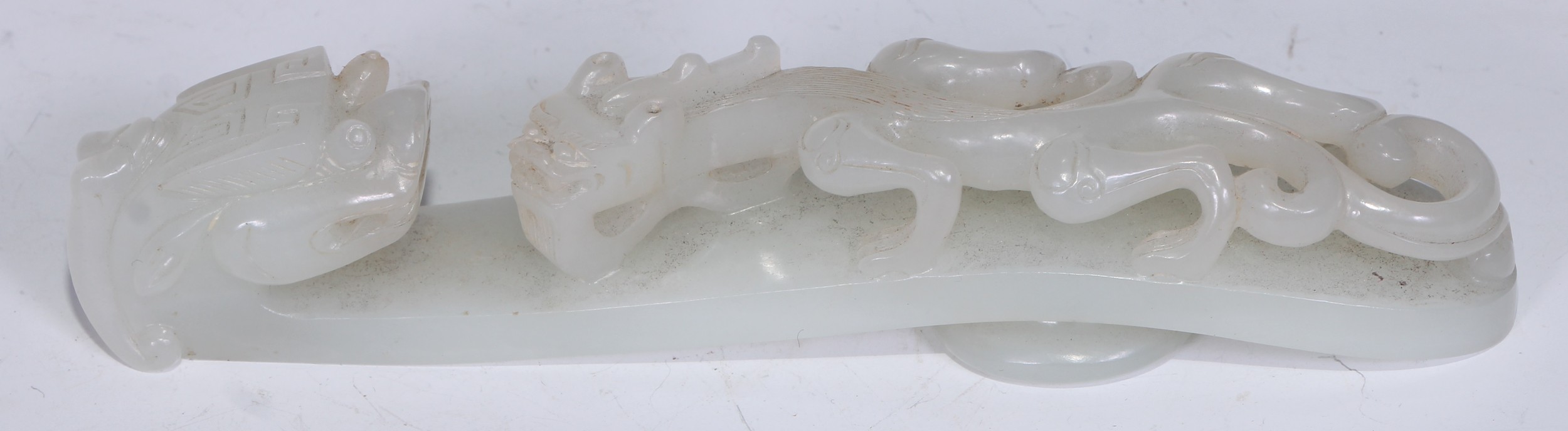 A Chinese pale celadon/white jade belt hook,  late Qing dynasty, of typical serpentine form, carved and pierced with chilong confronting the dragonhead terminal, 13cm long.