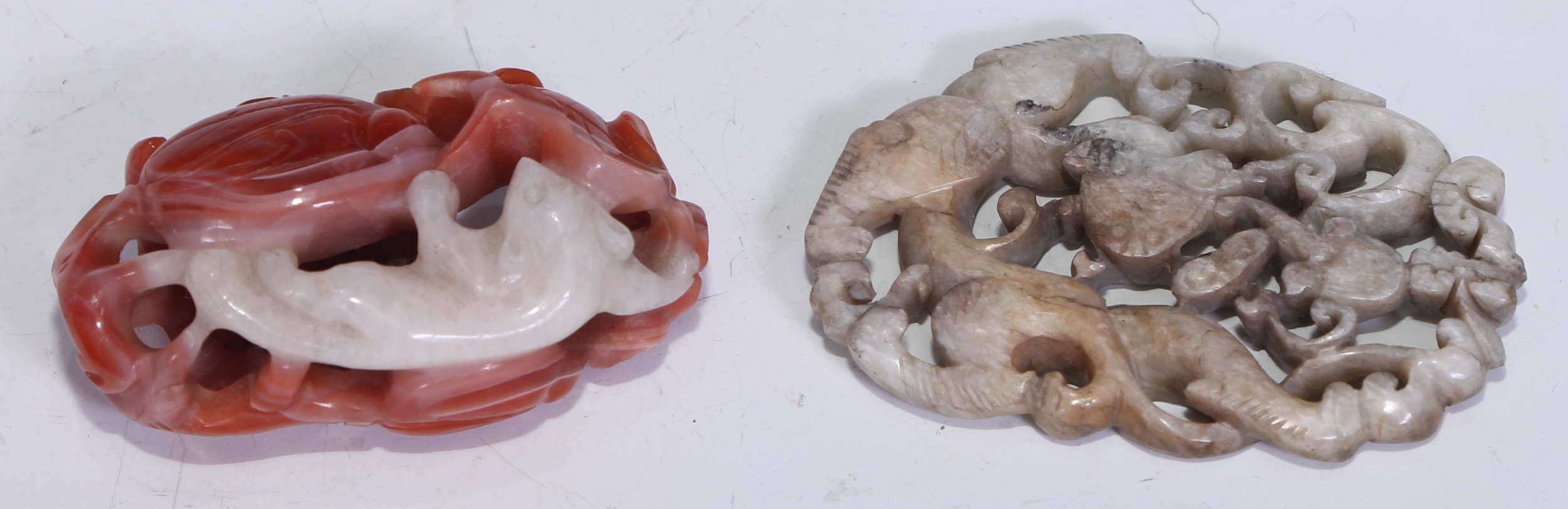 A Chinese oval pale jadeite panel, carved with Chilong amongst styalised scrolls, Qing dynasty, 5.5cm wide; a Chinese carved red and white agate pendant or toggle, carved and pierced with a cat amongst flowering lotus leaves, 5cm wide (2).