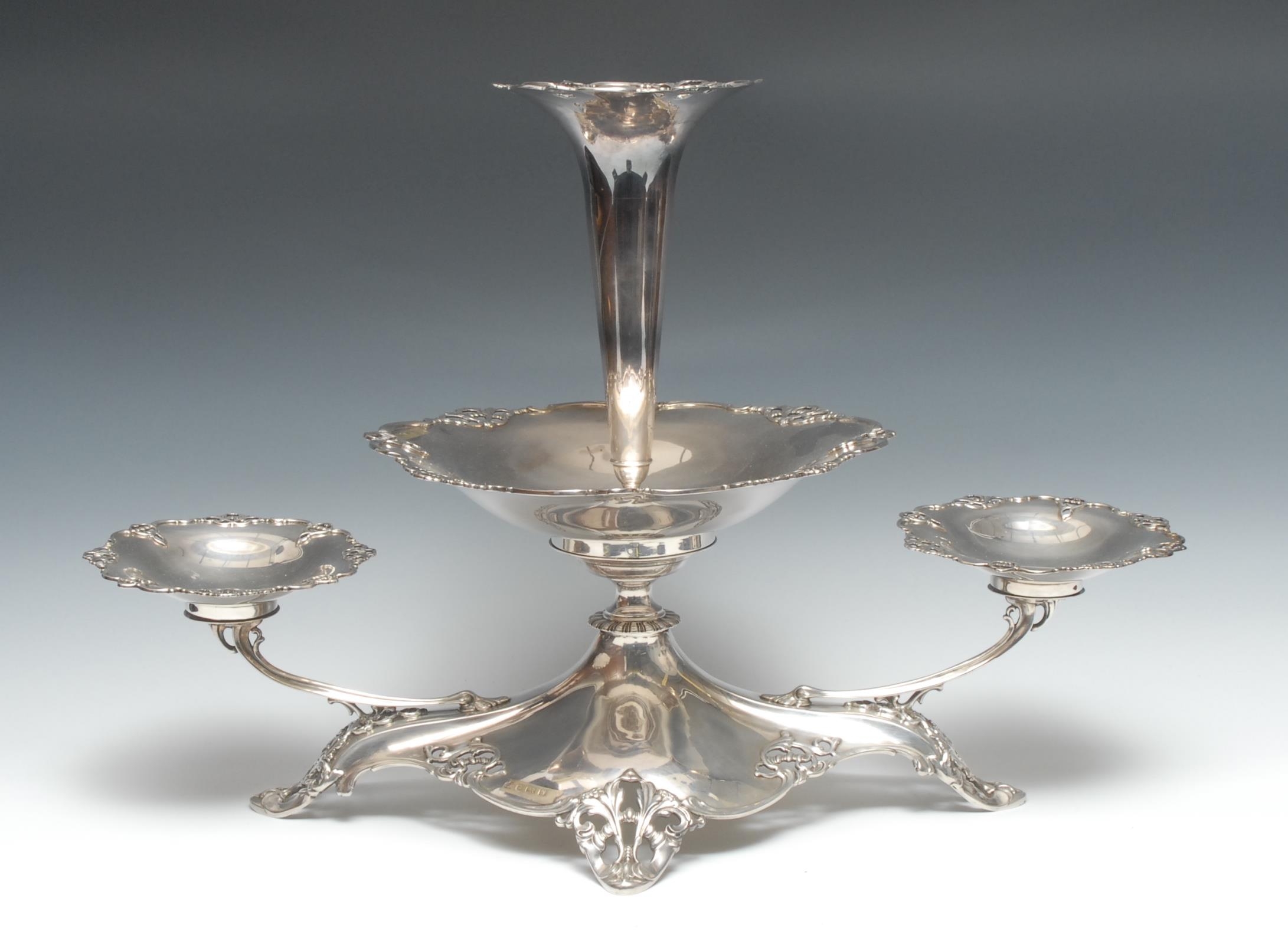 A large George V silver table epergne, central trumpet shaped flute above a shaped circular bowl, flanked by a pair of further sweetmeat dishes, domed quatrefoil base pierced and embossed with scrolling foliage, 38.5cm high, 56cm wide, Elkington & Co. Birmingham 1921, 1776g