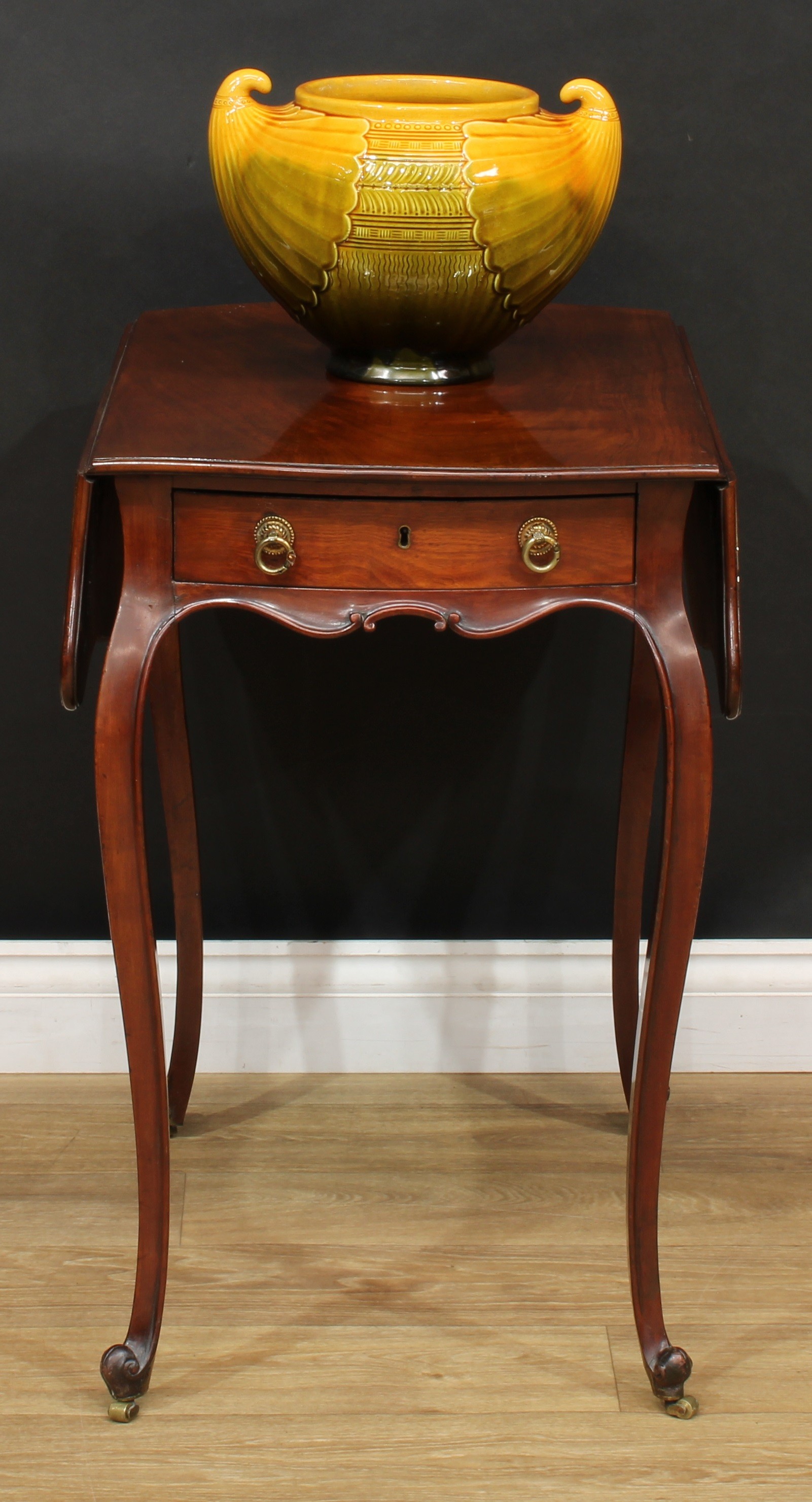 A George III mahogany Pembroke table, in the French Hepplewhite taste, butterfly shaped top with fall leaves above a frieze drawer, the verso conforming, French cabriole legs, scroll feet, brass barrel casters, 71.5cm high, 46cm opening to 81.5cm wide, 68cm deep, c.1780