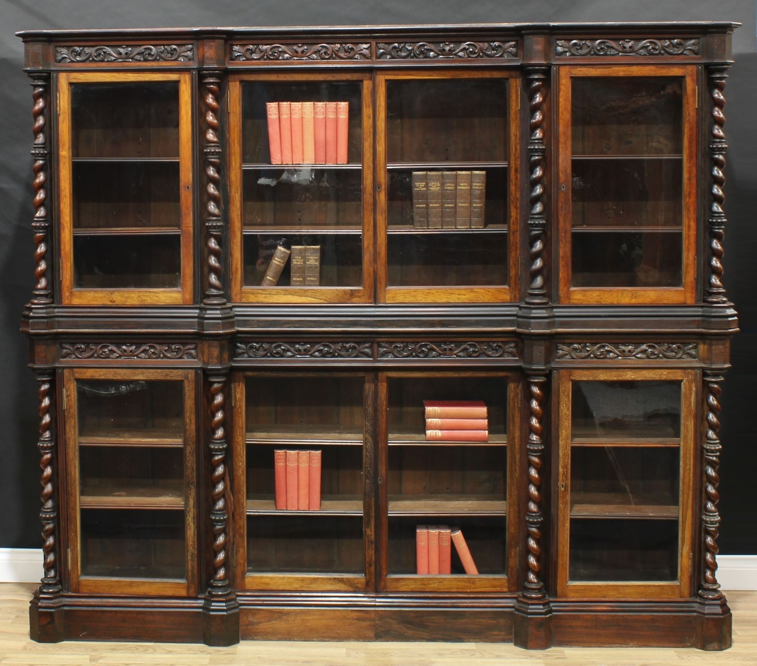A Victorian rosewood inverted break-centre library bookcase, deep frieze carved in relief with scrolling acanthus, above two pairs of rectangular glazed doors, divided and flanked by beaded spirally turned pillars, the base conforming, 190cm high, 217cm wide, 36cm deep, c.1860