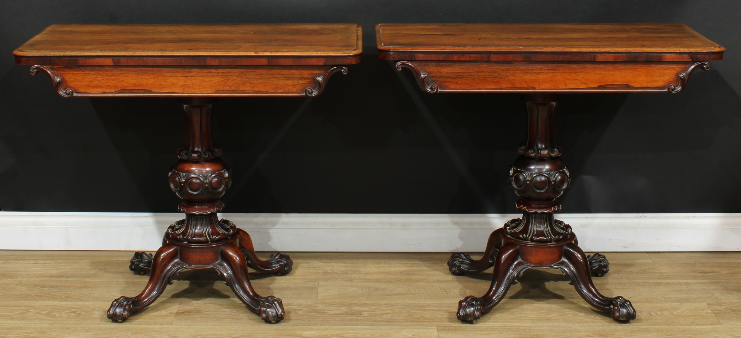 A pair of William IV rosewood tea tables, each with a hinged rectangular top above a frieze carved and applied with foliate S-scrolls, turned column carved and applied with scrolls and a chain of convex roundels, cabriole legs, ball and claw feet, brass casters, 76.5cm high, 92cm wide, 45cm deep, c.1835