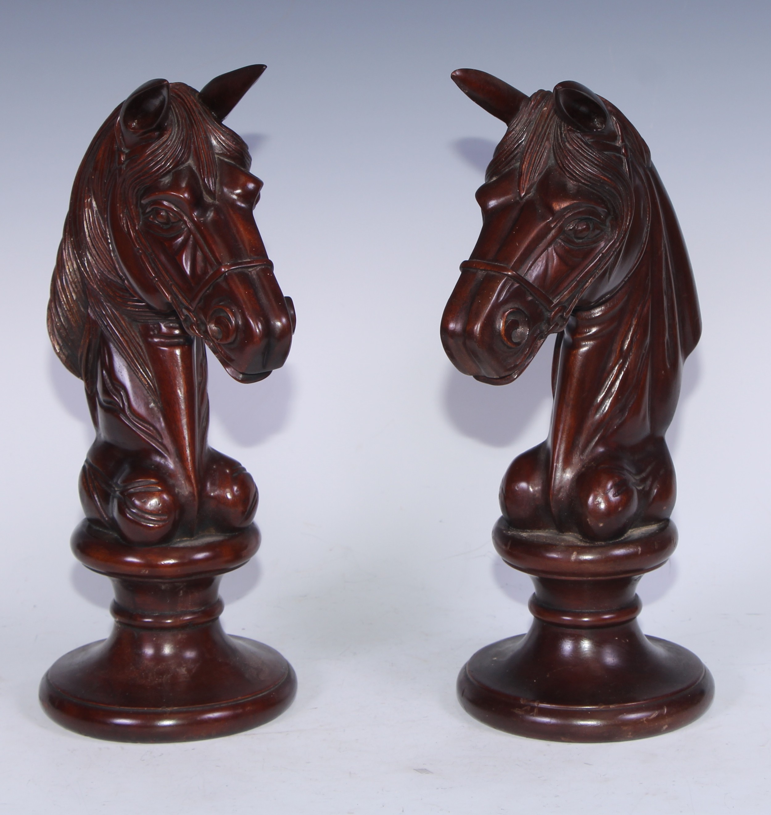 A pair of early 20th century mahogany oversize chess pieces, possibly advertising shop display models, each carved as a knight, waisted socles, 34cm high, c.1910