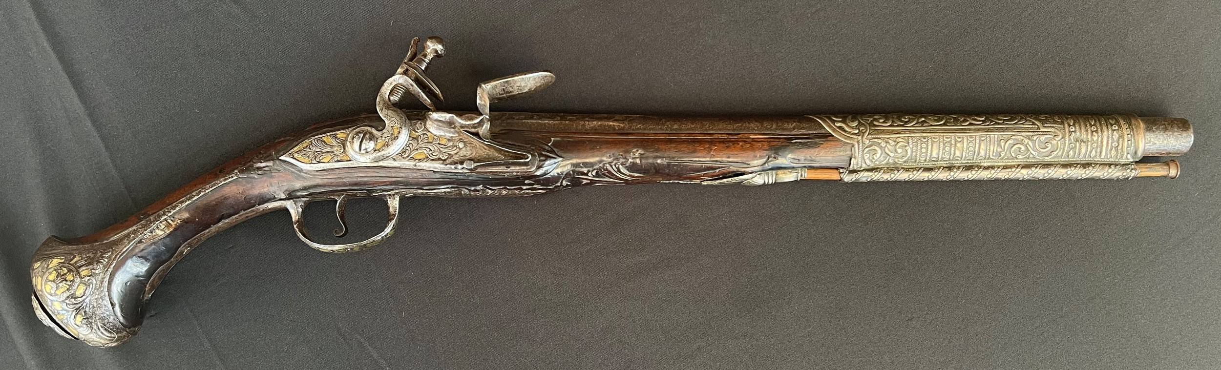 Flintlock Pistol with 360mm long barrel. Bore approx. 15mm. Overall length 548mm. Action will only hold at the half cocked position. Heavily decorated overall with cast brass and silver inlays. Complete with ramrod. No makers marks. Section 58 (2) no licence required.