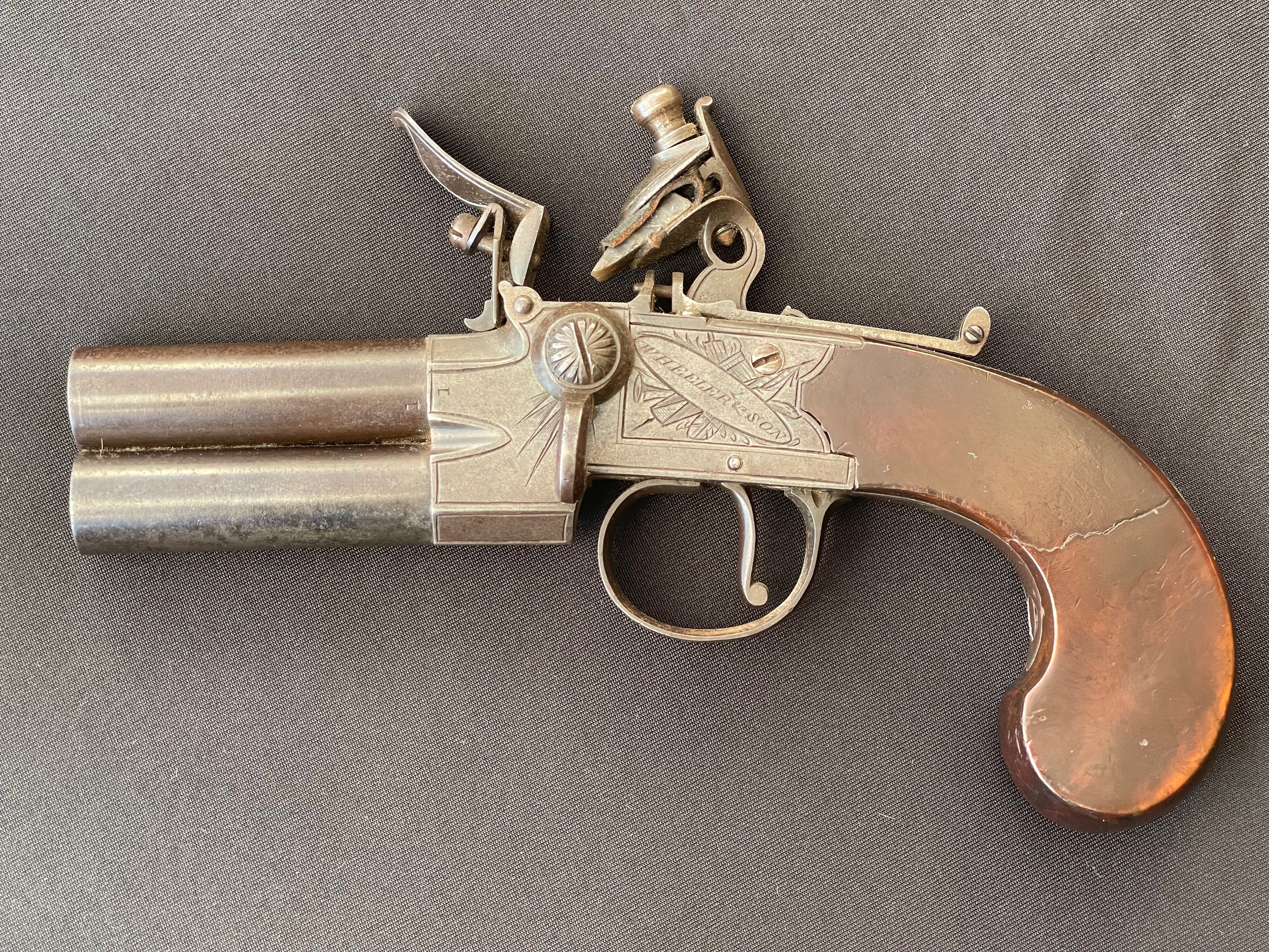 A scarce Double Barrel Over and Under Flintlock Tap Action Pistol by Wheeler & Sons London. 65mm long barrels. Engraved with makers mark and London along with piled arms. Working action which holds at both full and half cocked positions. Working safety catch. Butt is inset with a blank silver escutcheon plate. Clear English Proof marks. Overall length 185mm. Section 58 (2) no licence required.