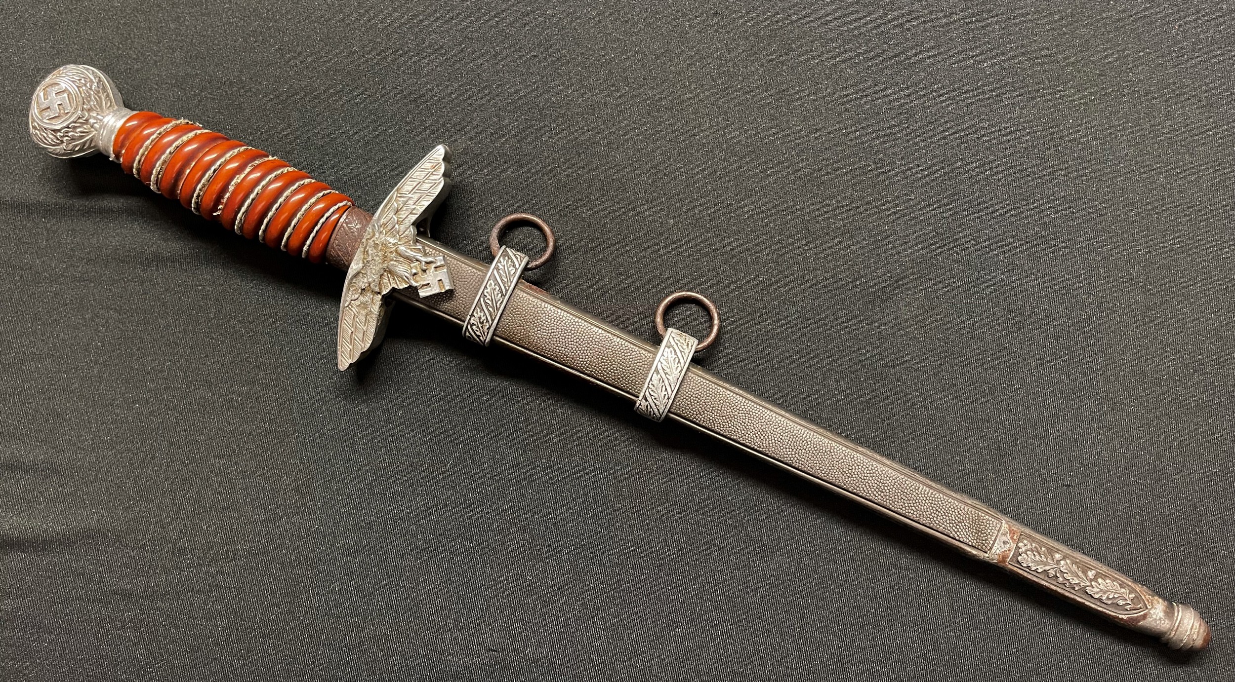 WW2 Third Reich Luftwaffe Dagger with double edged blade 255mm in length maker marked "SMF, Solingen". Also Luftwaffe Proof mark Eagle 5 to blade. Orange grip with partial grip wire present. Overall length 385mm. Complete with steel scabbard with alloy fittings.