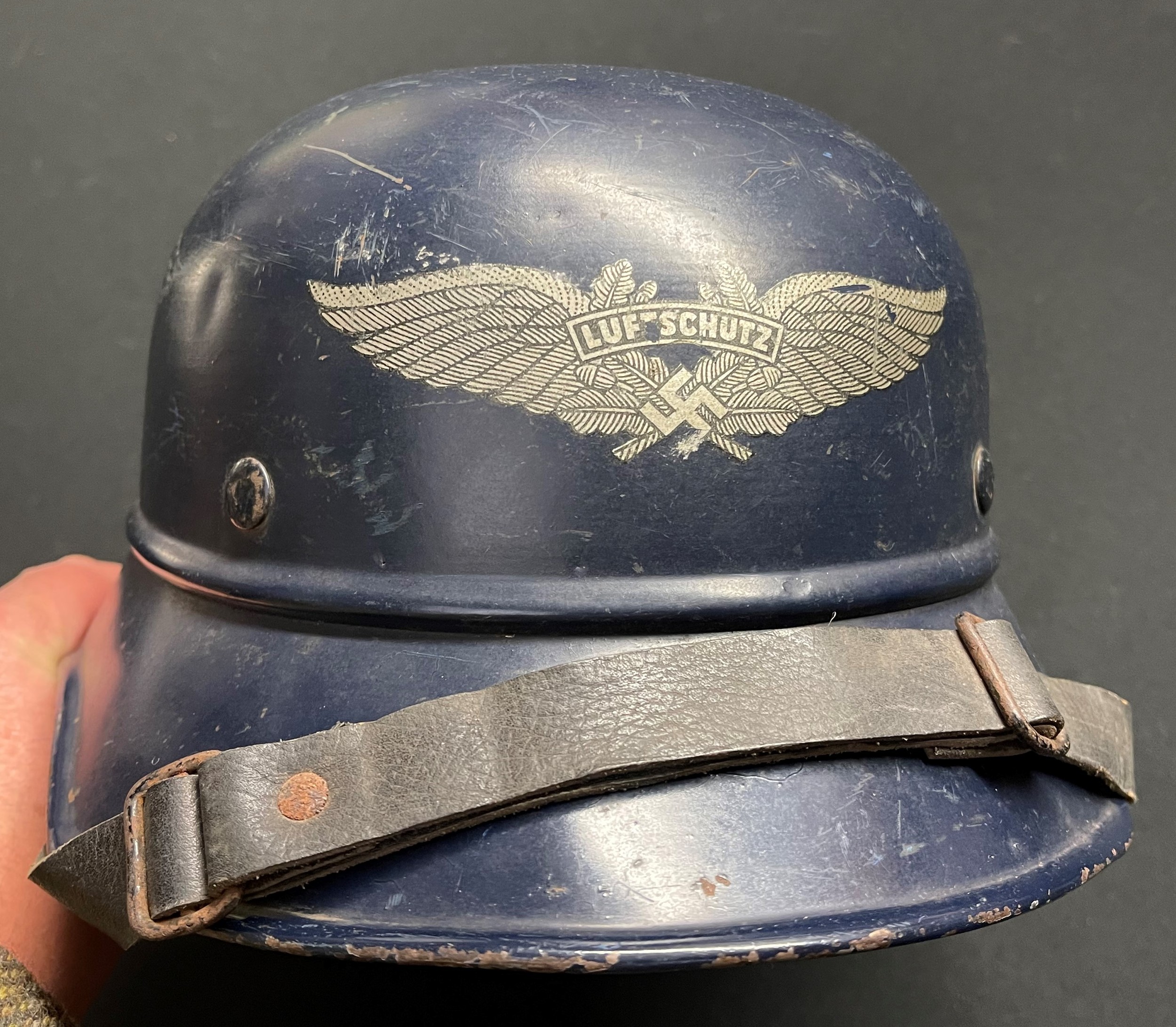 WW2 Third Reich Luftschutz M38 Steel Helmet. Original blue paint and decal. Complete with original liner, drawstring and chinstrap. Shell is marked "RL 2 - 38/28" along with original size and price decal. Size 56. Leather liner is also marked with the original lady owners name.