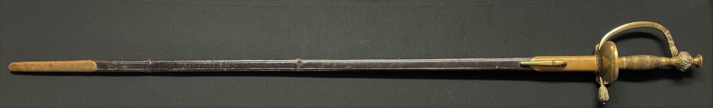 European Small sword with etched fullered single edged blade 805mm in length. Etched with Crown over an Imperial Eagle on one side and piled arms on the opposite side. No makers mark. Folding double shell brass guard. Wire bound grip. Overall length 950mm. Complete with leather scabbard with brass throat with frog stud plus brass chape.