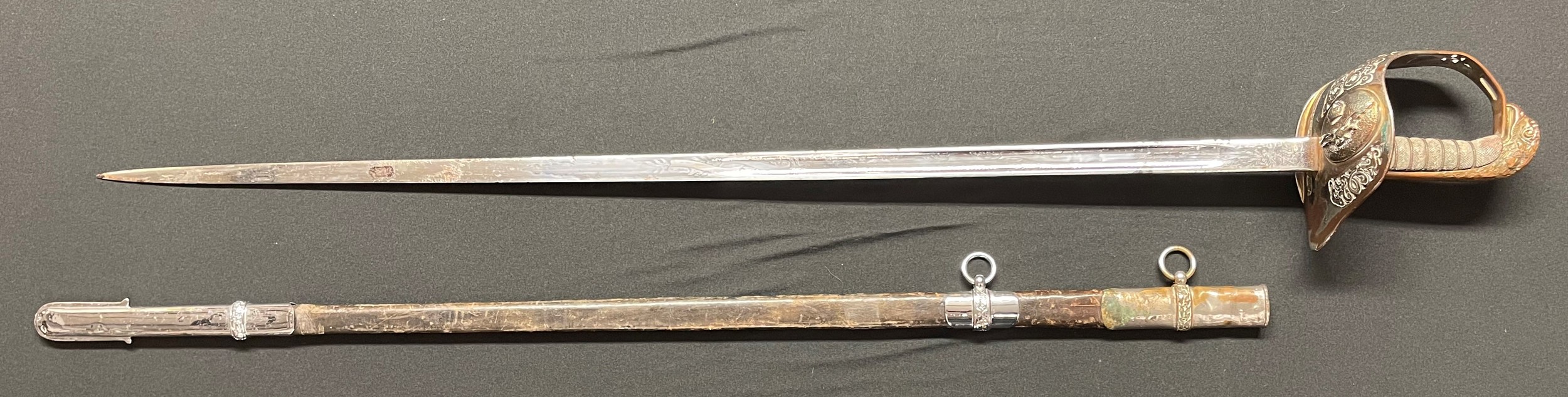 ERII RAF Officers Sword with 82cm long fullered blade with worn heavy chrome plating. Marked "Made in England" . RAF Eagle to Guard with Kings Crown above. ERII Cypher. Wire bound shagreen grip. Overall length 96cm. Complete with leather scabbard with heavily plated fittings.