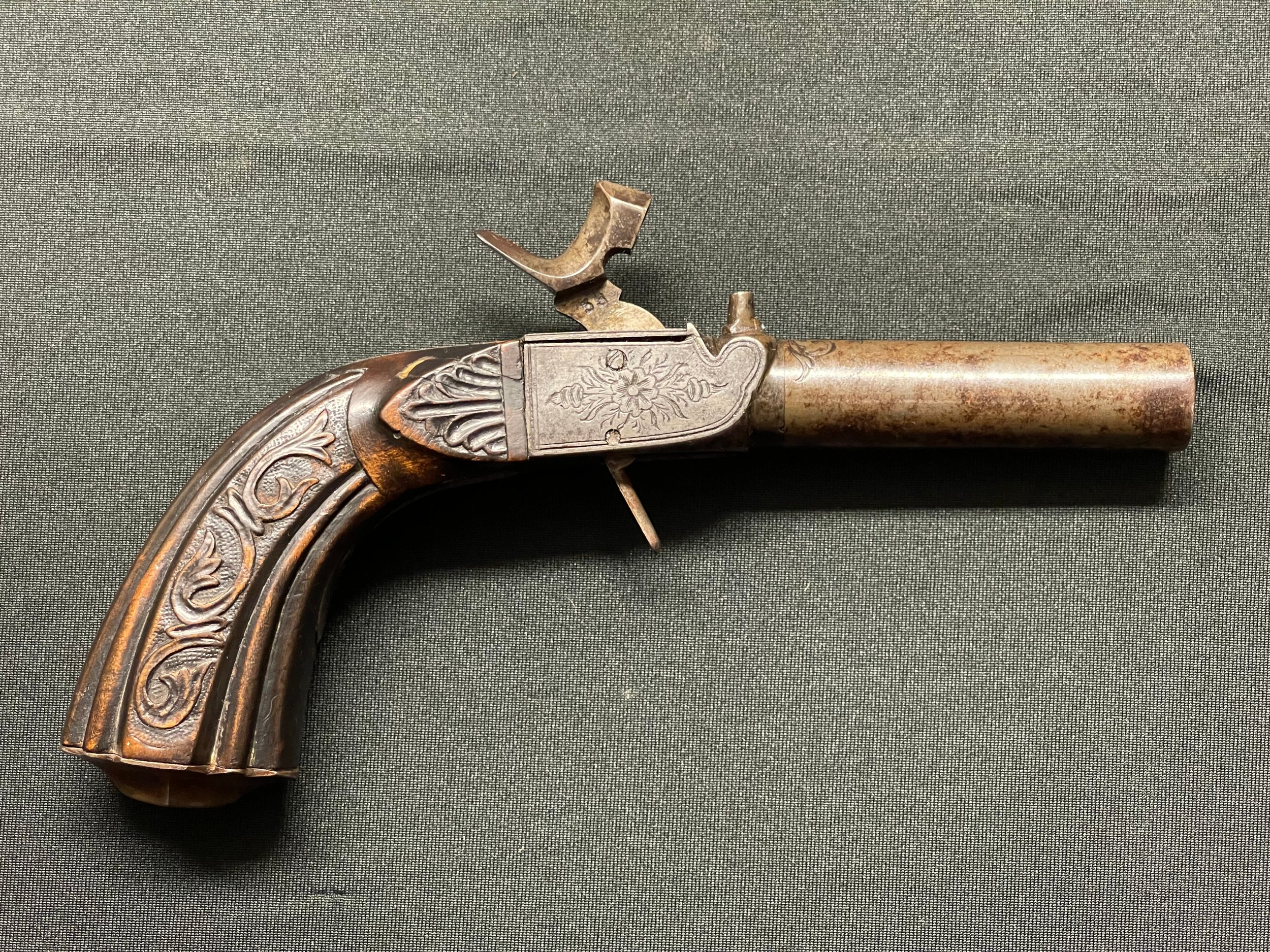 Percussion Cap Pocket Pistol with 62mm long barrel. Bore approx. 12mm. Unsigned. Barrel, hammer and lock all marked "38". Folding trigger. Working action, holds at both full and half cocked positions. Engraved Floral decoration to lock and trigger. Carved decoration to wooden butt. No makers marks or Proof marks. Overall length 173mm. Section 58 (2) no licence required.