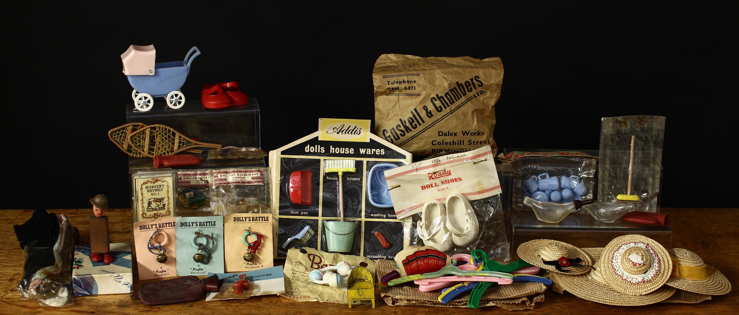 A collection of doll and dolls house miniatures, curios and accessories, first-half 20th century and later, comprising Addis dolls house wares miniatures including dust pan, house broom, washing bowl, hand brush, pail and scrubbing brush, sealed on cardboard backing; three “Maylen” dolly’s rattle, each displayed on coloured backing paper; a Fairylite miniature hot water bottle; a pair of 1950’s Roddy doll shoes, size 2, in packet with cardboard header; a ‘grip-tight’ dolly soother, in packet on cardboard backing; Folk-Art novelty miniature painted wooden figure in the form of a soldier, the body made from a rounded rectangular rubber or eraser, 7cm high; various novelties in brown paper bags from Beales, Bournemouth; other dolls house accessories in packets including Dol-Toi Glassware, Stamford etc (quantity)