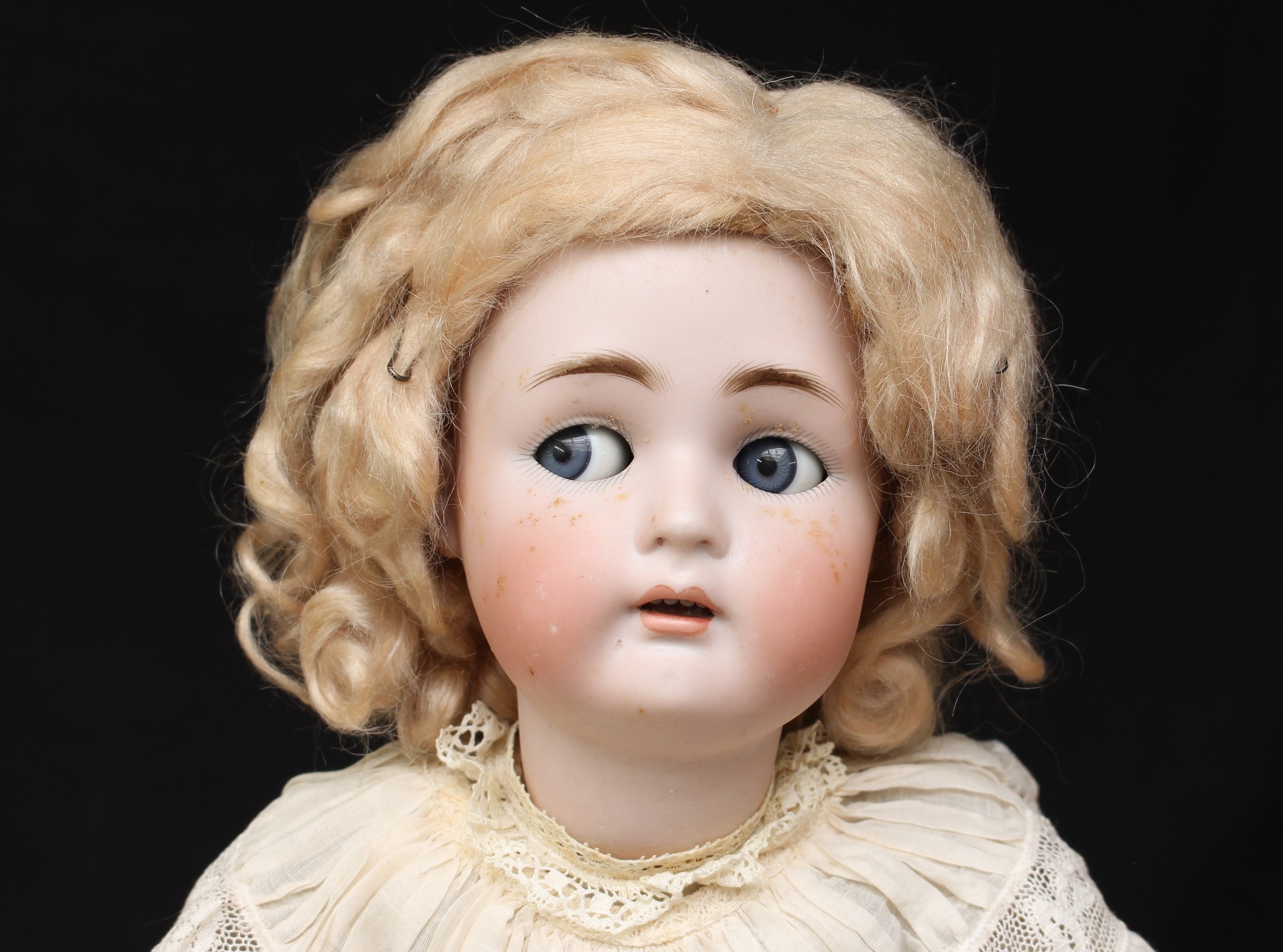 A Simon & Halbig/Kammer & Reinhardt (Germany) bisque head and ball jointed painted composition bodied doll, weighted sleeping and side glancing blue glass eyes, painted features including feathered eyebrows and fine eyelashes, open mouth revealing upper teeth, pierced ears, blonde wig, impressed marks 'SIMON & HALBIG K&R 55', wearing a white linen dress with underclothes, 52cm high