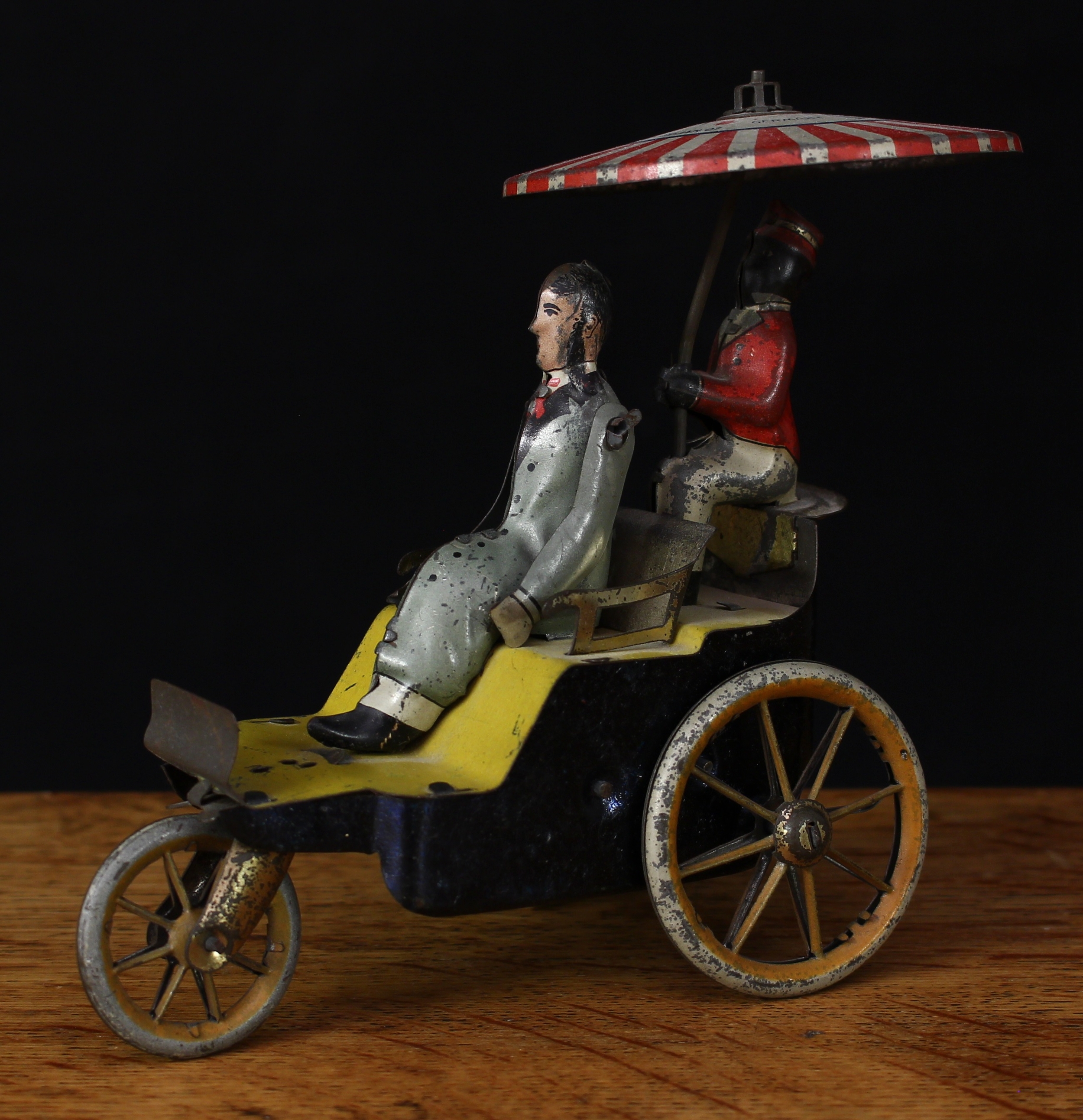 An early 20th century Lehmann (Brandenburg, Germany) EPL345 New Century Cycle novelty tinplate and fixed key wind automaton toy, comprising seated rider and attendant upon a three wheeled cycle, the attendant holding a parasol, 14cm high, unboxed, c.1902