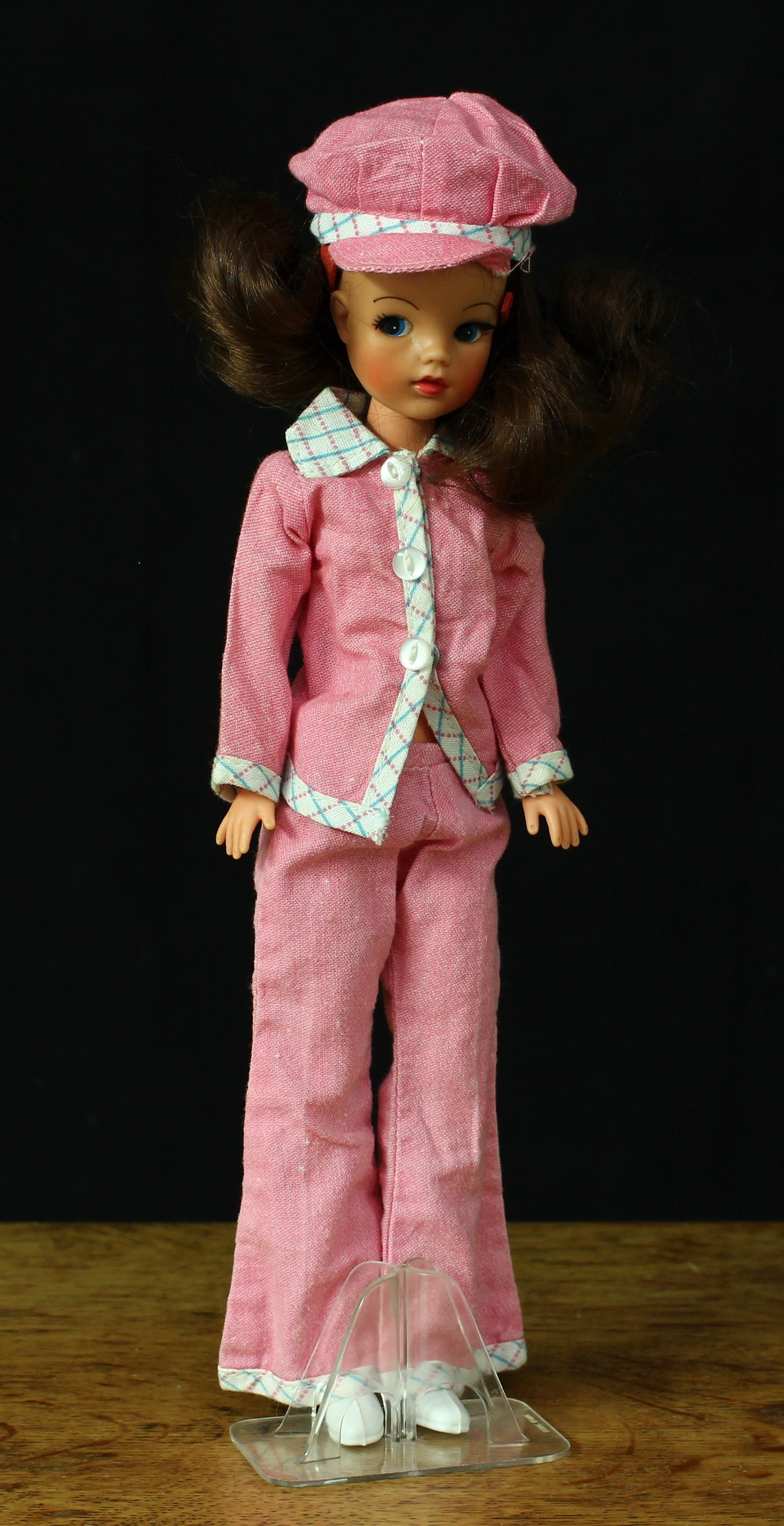A 1970’s Sindy doll, auburn/brunette hair, side glancing blue eyes, wearing a pink outfit with flared trousers and peak cap, white boots, marked ‘033055X’ to back of head, ‘033029’ to upper back and ‘033030’ to below lower back, 28cm high, unboxed with clear plastic display stand