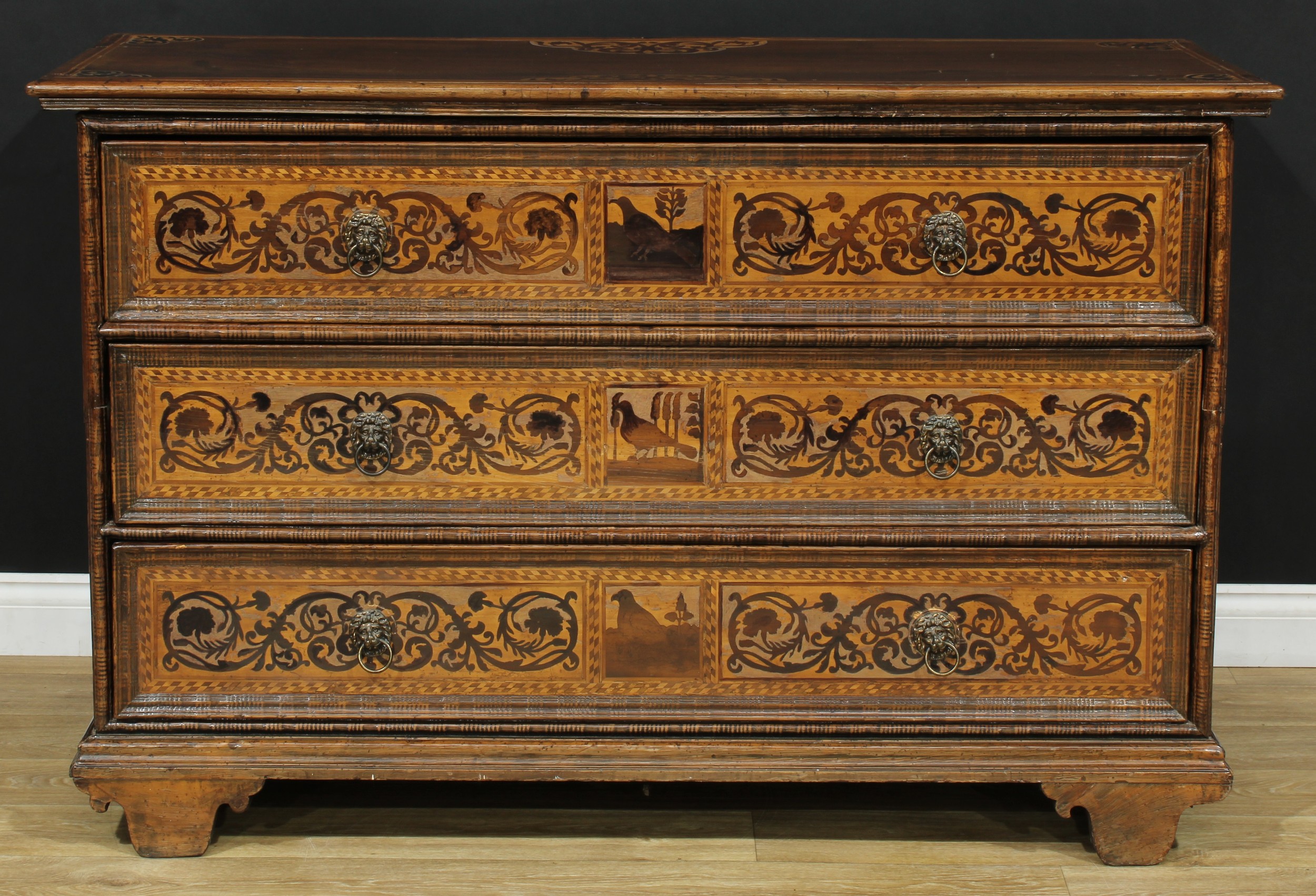 A German marquetry chest, oversailing rectangular top above three long drawers, lion mask ring handles, inlaid with animals, scrolling leaves and flowers, the drawer fronts outlined throughout with barber-pole stringing, skirted base, 92cm high, 145cm wide, 58cm deep