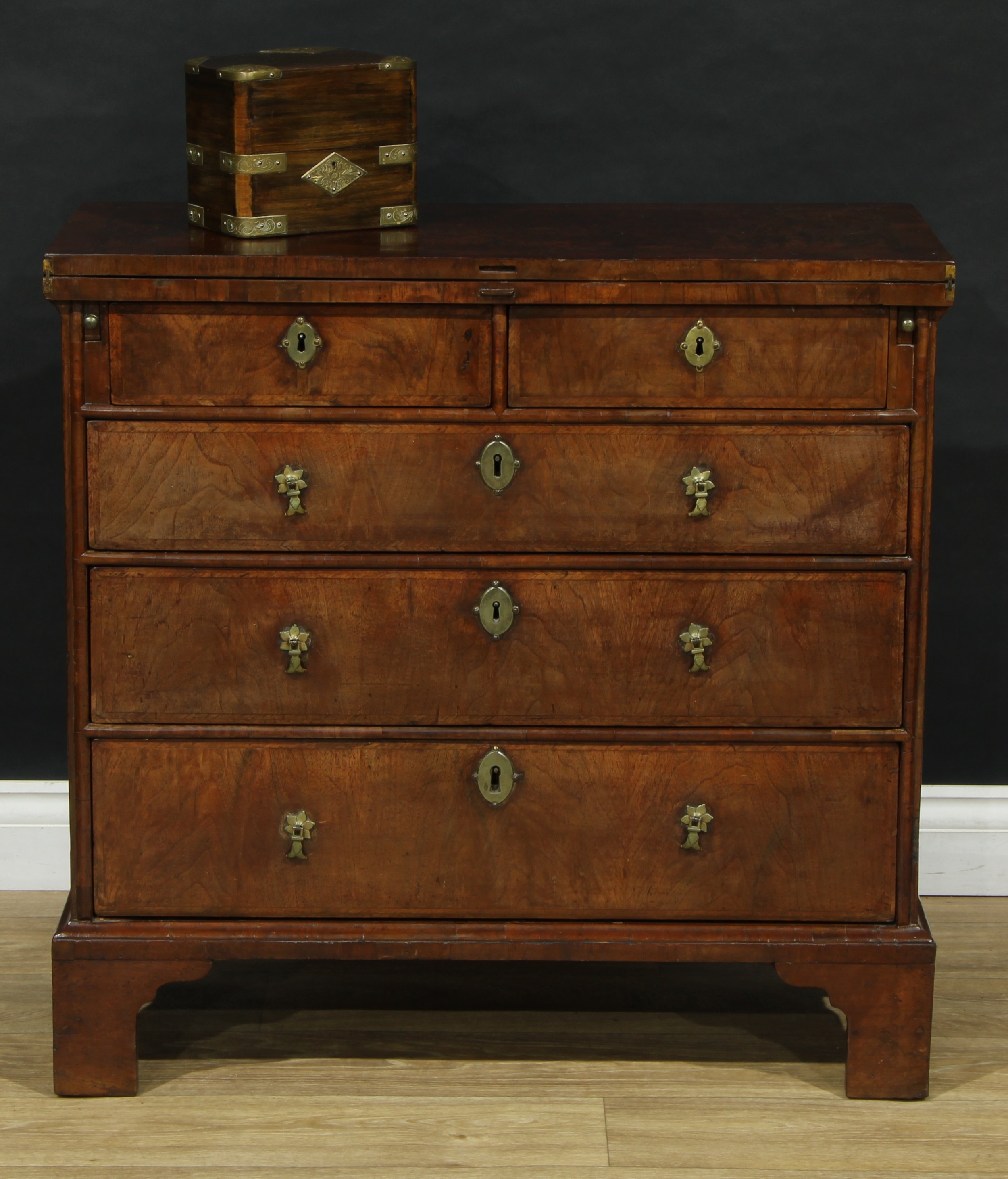 A Queen Anne walnut bachelor's chest, of small proportions, crossbanded fold-over top with matched veneers, above two short and three long graduated drawers, outlined throughout with herringbone stringing, brass drop handles, skirted base, bracket feet, 79.5cm high, 81.5cm wide, 35cm deep, c.1710