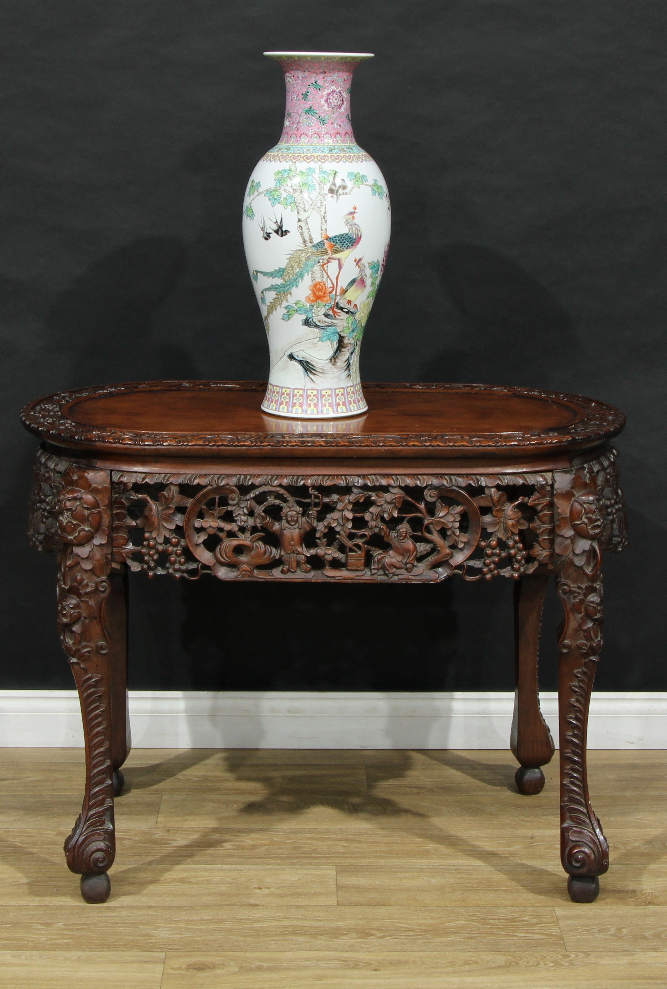 A Chinese hardwood oval centre table, panel top carved with a border of flowers, above a pierced frieze of fruiting vine, square cabriole legs, knop feet, 81cm high, 105cm wide, 61cm deep, early 20th century