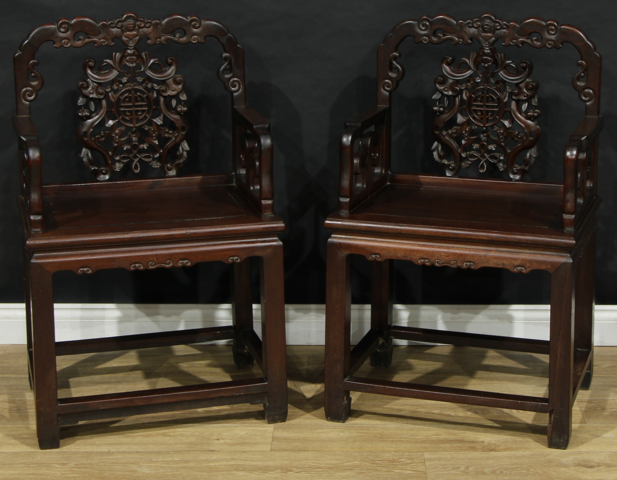 A pair of Chinese hardwood armchairs, each shaped back with pierced splat carved with bats, double-happiness and fruiting foliage, panel seats, square legs, 98cm high, 62cm wide, the seat 52cm wide and 42cm deep, early 20th century