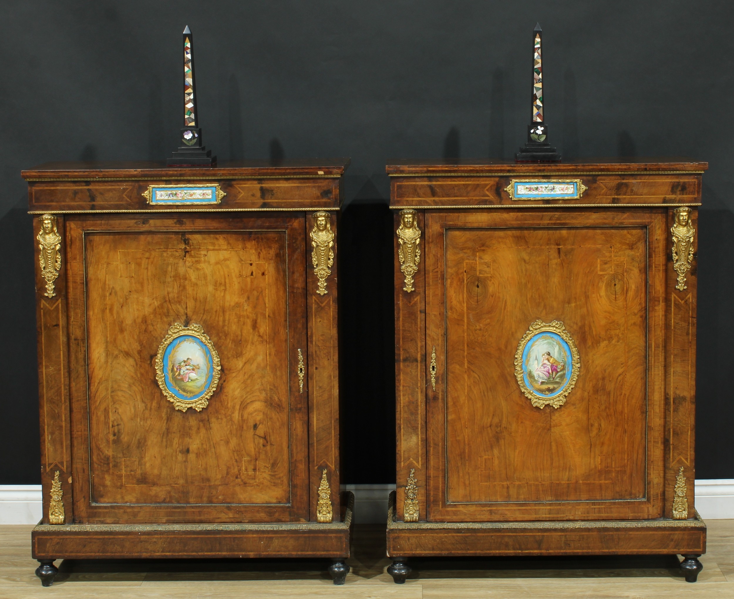 A pair of Victorian gilt metal and porcelain mounted walnut pier cabinets, slightly oversailing rectangular tops above rectangular doors applied with panels painted in the manner of Sevres on a bleu celeste ground, outlined throughout with geometric banding and boxwood stringing, plinth bases, turned feet, 107.5cm high, 81cm wide, 37cm deep, c.1870