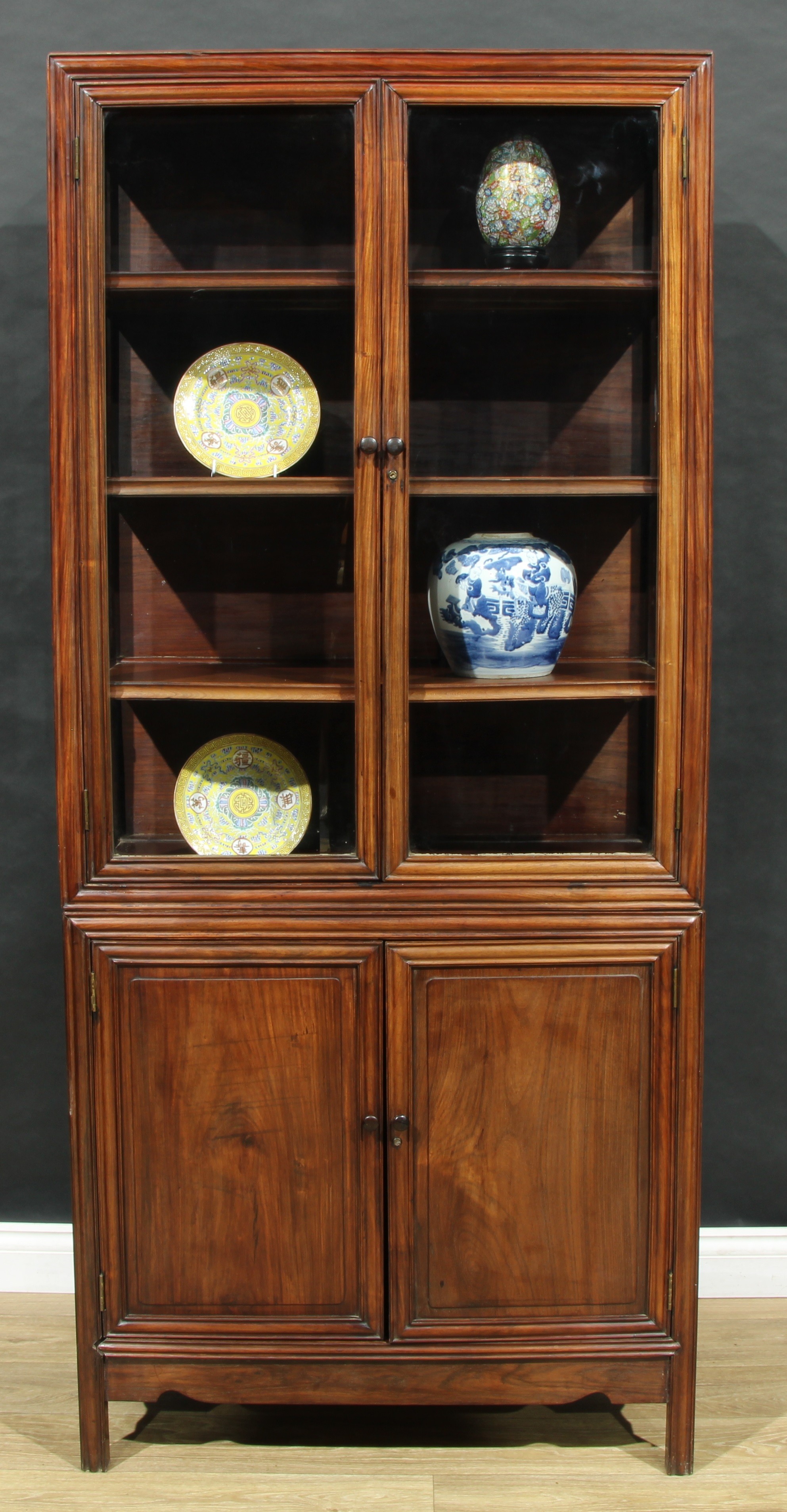A Chinese hardwood porcelain display cabinet, quite plain, rectangular glazed doors enclosing shelves, the base with a pair of panel doors, 189cm high, 83.5cm wide, 35cm deep, early 20th century