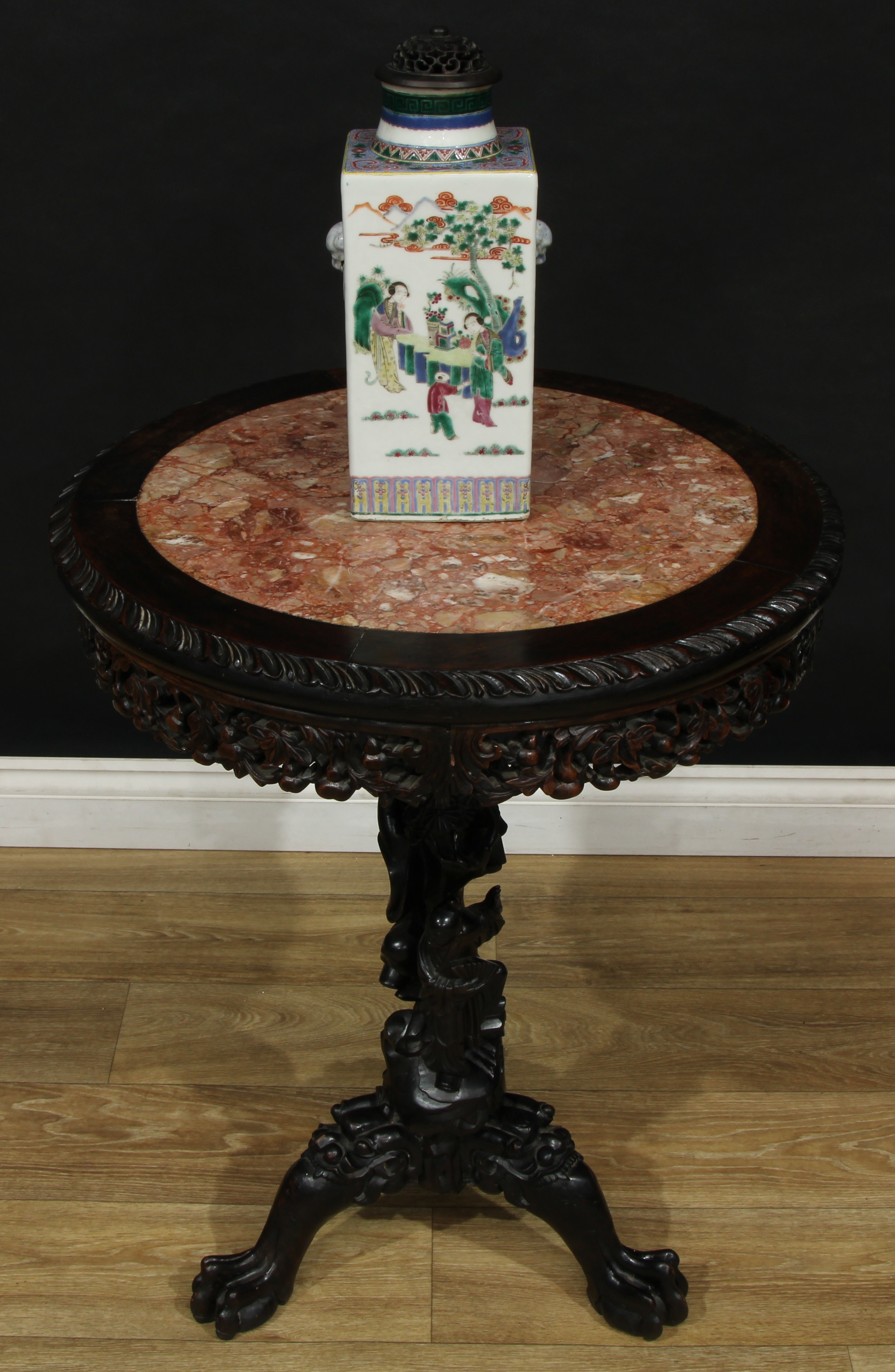 A Chinese hardwood tripod occasional table, circular top with inset soapstone panel, the pillar carved with smiling figures holding a fan and a censer, on a ground of scrolling and fruiting foliage, cabriole legs with masks to knees, ball and claw feet, 78cm high, 56cm diameter, c.1860