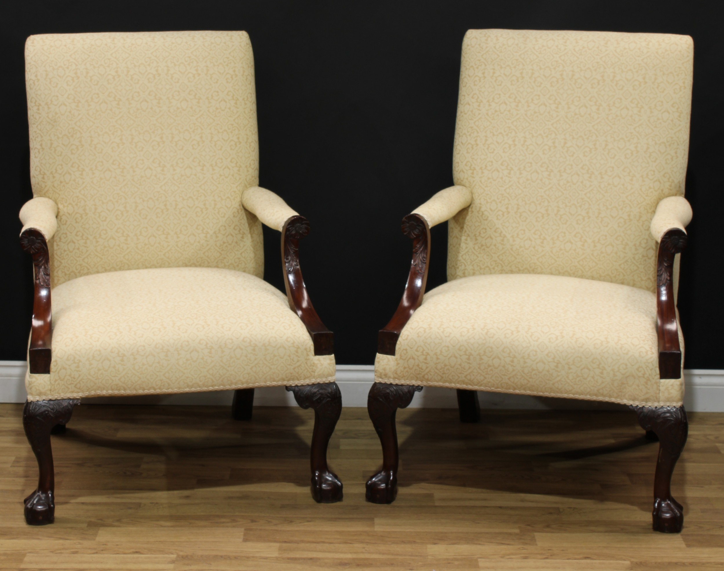 A pair of 19th century mahogany Gainsborough armchairs, each with a rectangular back, scroll arms carved with a flowerhead boss and acanthus, stuffed-over upholstery cabriole forelegs carved to the knees with further acanthus, ball and claw forefeet, one 108cm high, 74.5cm wide, the seat 48cm wide and 46cm deep, the other 107cm high, 74.5cm wide, the seat 50cm wide and 47cm deep (2)
