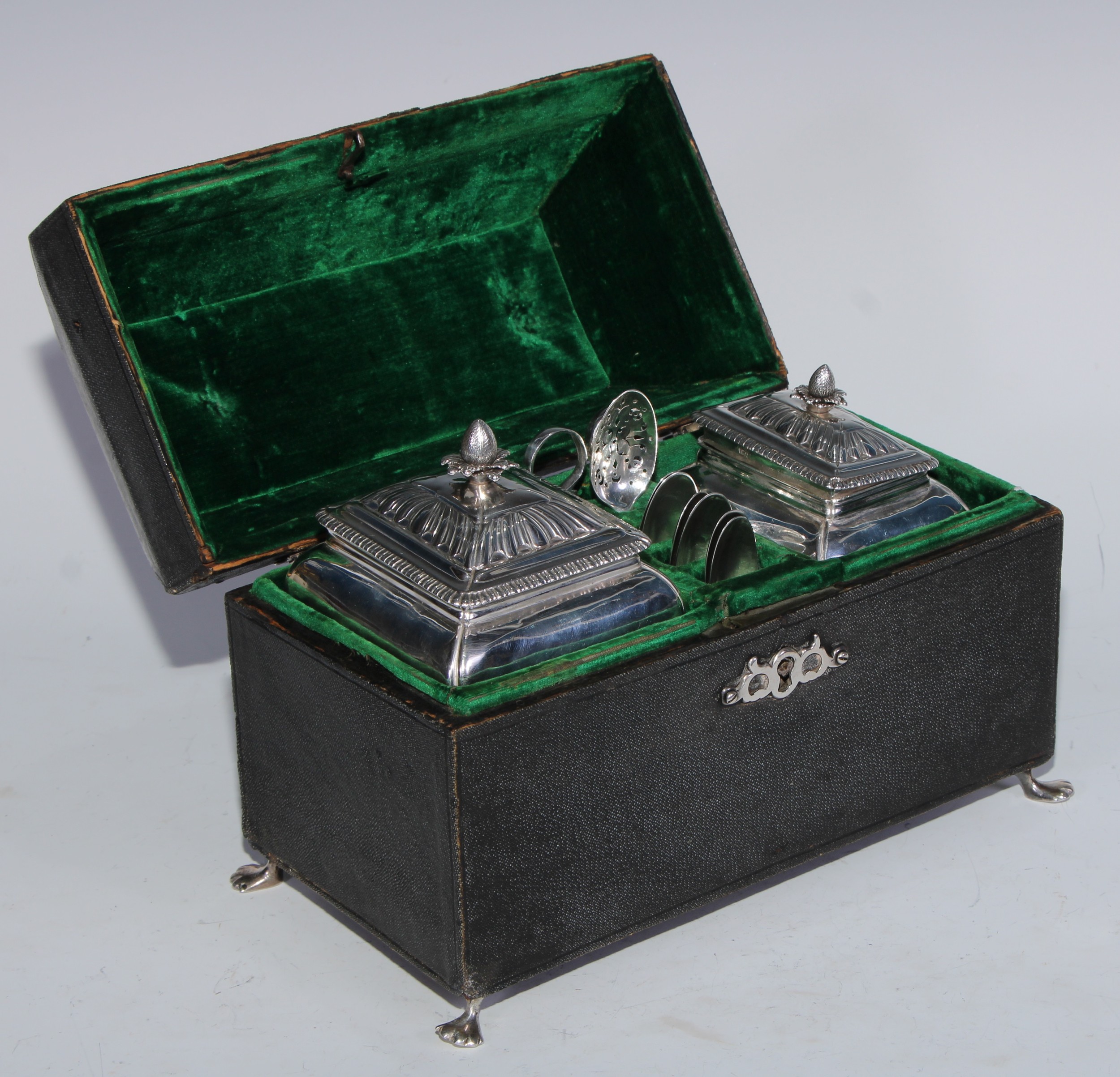 A George II silver tea caddy and sugar box, each with batwing-fluted domed cover, gadrooned borders, shell aprons and scroll feet, the caddy 14cm high, Pierre Gillois, London 1759, 564g, cased en suite with associated mote spoon, a set of six Hanoverian tea spoons and a pair of sugar tongs, the shagreen sarcophagus box with swing handle, pierced escutcheon and paw feet, 23cm wide