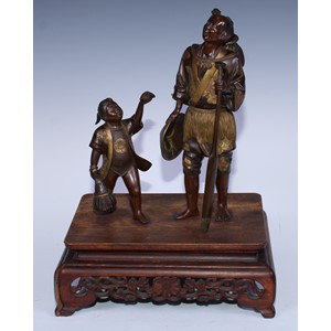 A Japanese brown and gilt patinated bronze group of a Cormorant fisherman and boy, he stands holding an oar with the bird resting on the creel on his back, the boy offers a terrapin, hardwood base, 40cm high overall