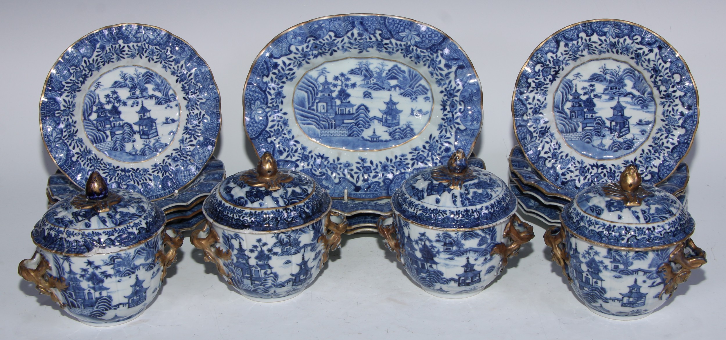 A Chinese table service, comprising four fluted oval plates, ten circular dishes and four bowls and covers, each decorated in underglaze blue with pagodas in a monumental landscape, the oval plates 24.5cm wide, Qianlong rein, c.1770 (18)