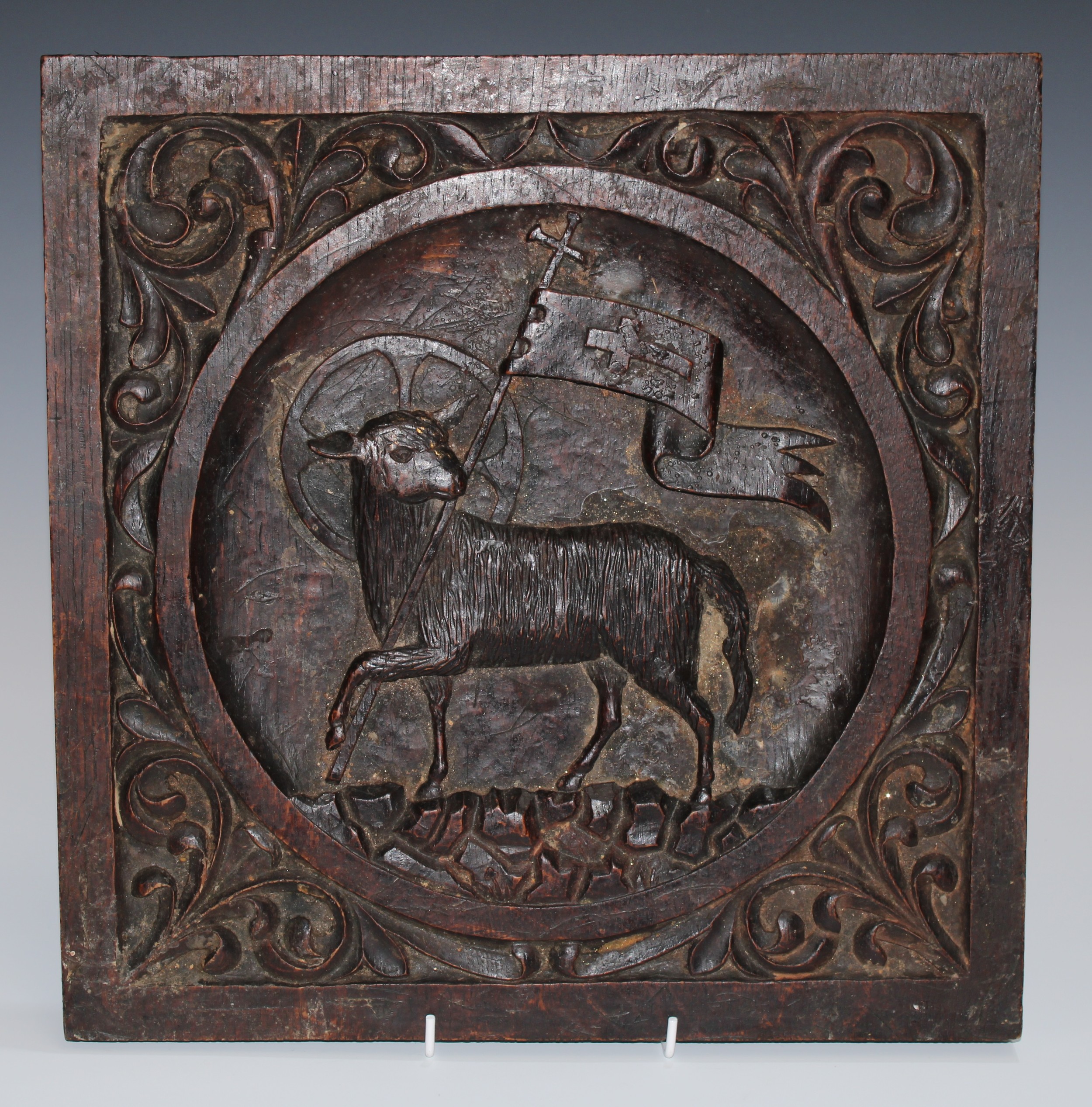 A North European oak panel, carved with Agnus Dei, within a tondo, the spandrels with scrolling acanthus, 36cm x 35.5cm, 19th century