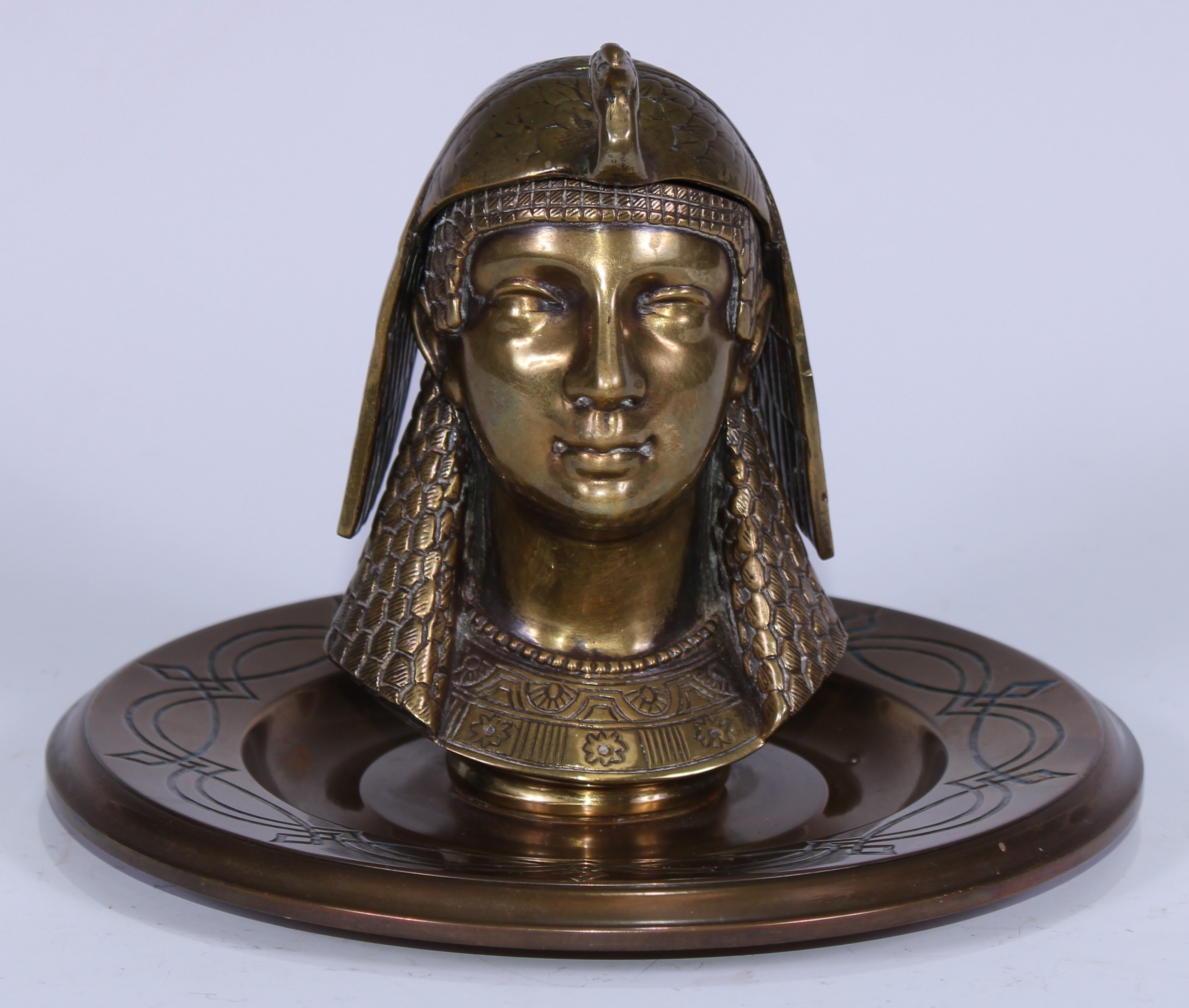 A 19th century Egyptian Revival gilt brass inkwell, cast as the head of a noblewoman wearing a peacock headdress, 18.5cm diam, c.1870
