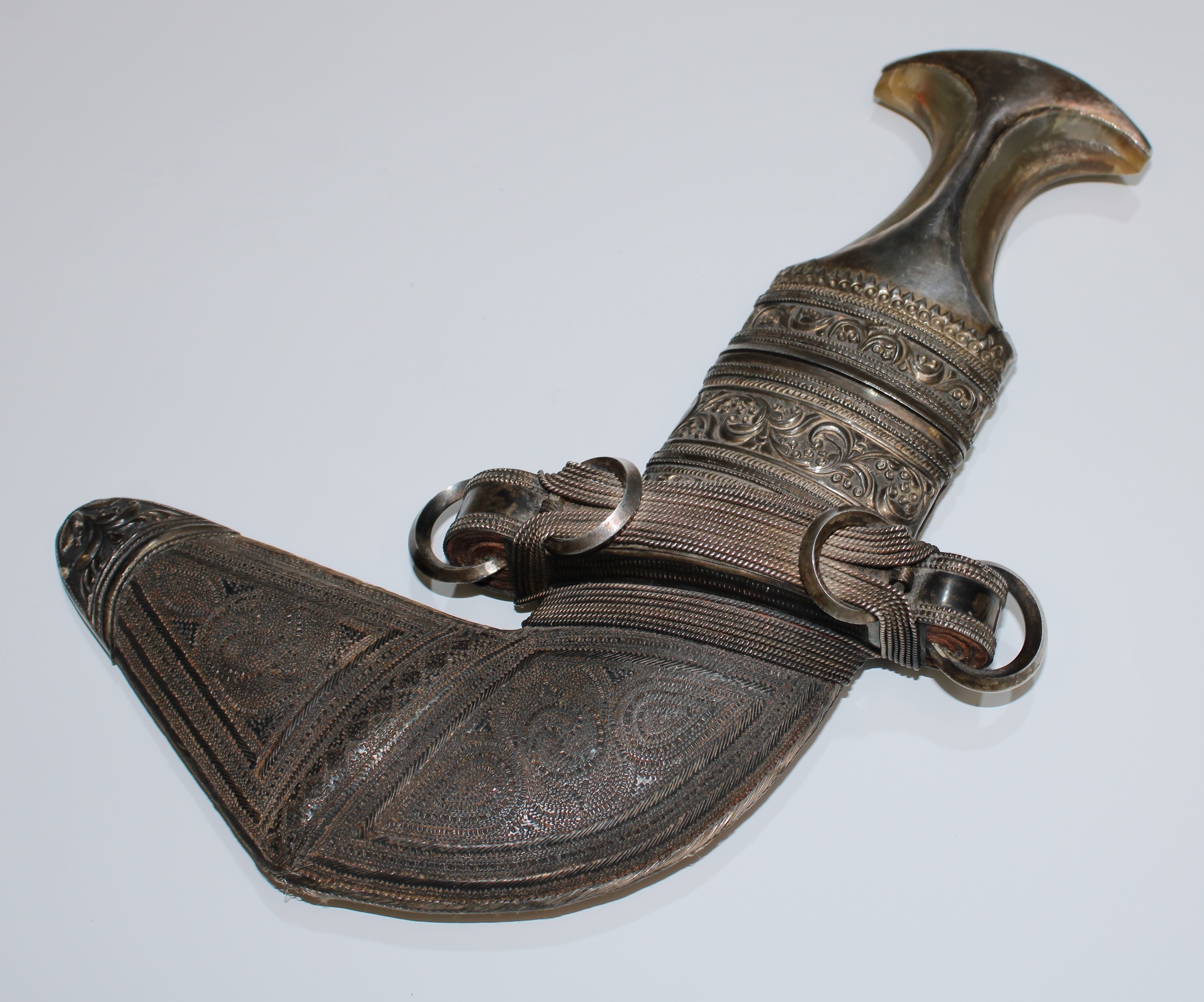 A Middle Eastern silver mounted jambiya dagger, 17cm curved blade with central ridge, horn grip, the leather scabbard with chased and woven filigree mounts, 28cm long, 19th/early 20th century