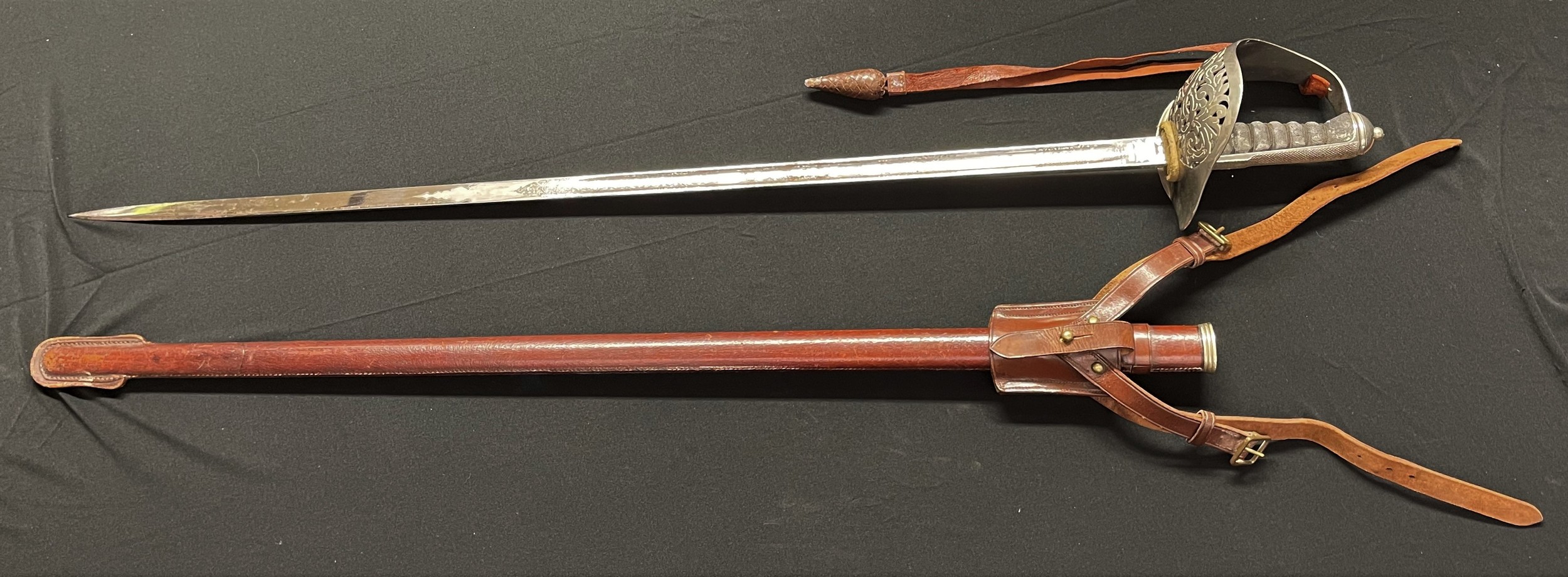 WW2 British Army Officers 1897 Pattern Sword with etched decorated fullered blade 822mm in length with proof mark, and "Wilkinson Sword Co. Ltd, London" makers mark. Spine of blade marked "Made in England" along with serial number 67988. White felt buffer pad. Wire bound shagreen grip. Guard marked "GRI". Overall length 990mm. Complete with original leather knot. Complete with leather covered scabbard and leather frog for the Sam Brown Belt.