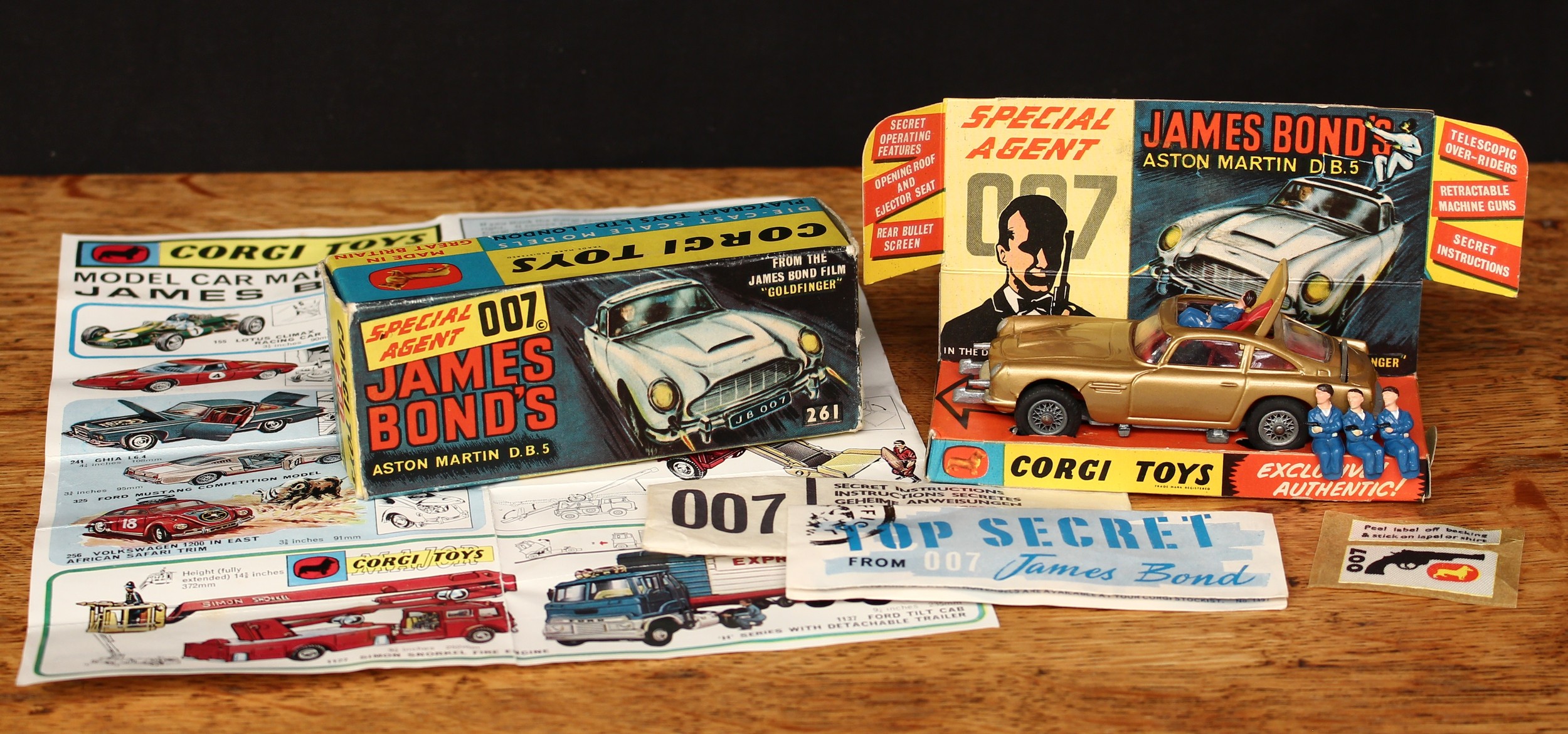 Corgi Toys 261 Special Agent 007 James Bond’s Aston Martin D.B.5 from the James Bond film “Goldfinger”, gold body with red interior, wire spoke wheels, James Bond and seated plastic bandit figures to interior, boxed with original inner cardboard pictorial display stand, 007 secret instructions packet with instructions, three spare plastic figures, unused lapel badge on backing sheet and Corgi Toys collector’s check list literature