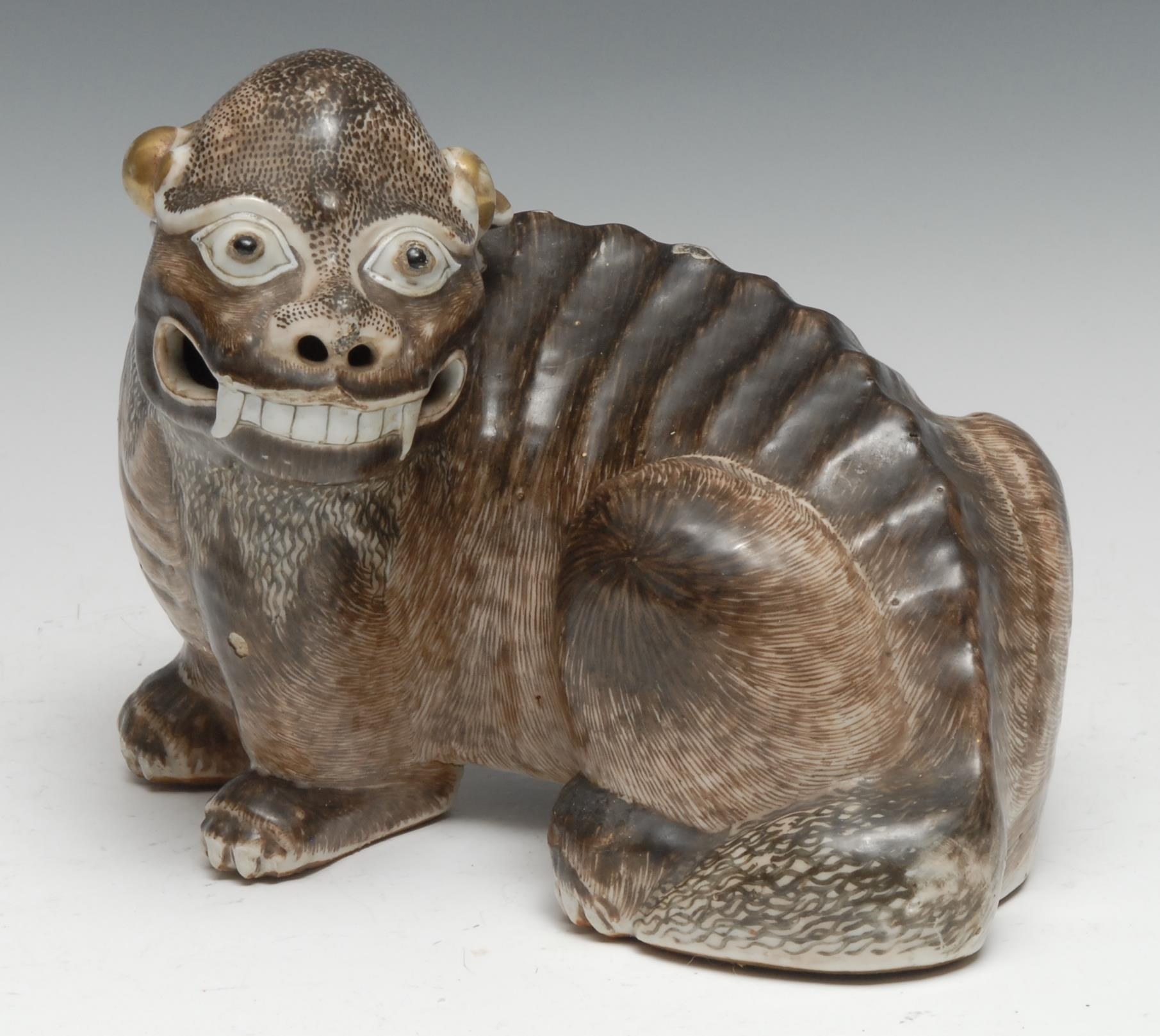 A Chinese porcelain model, of a Dog of Fo, typically modelled and picked-out in naturalistic tones, gilt ears, 22cm long, 19th century or earlier