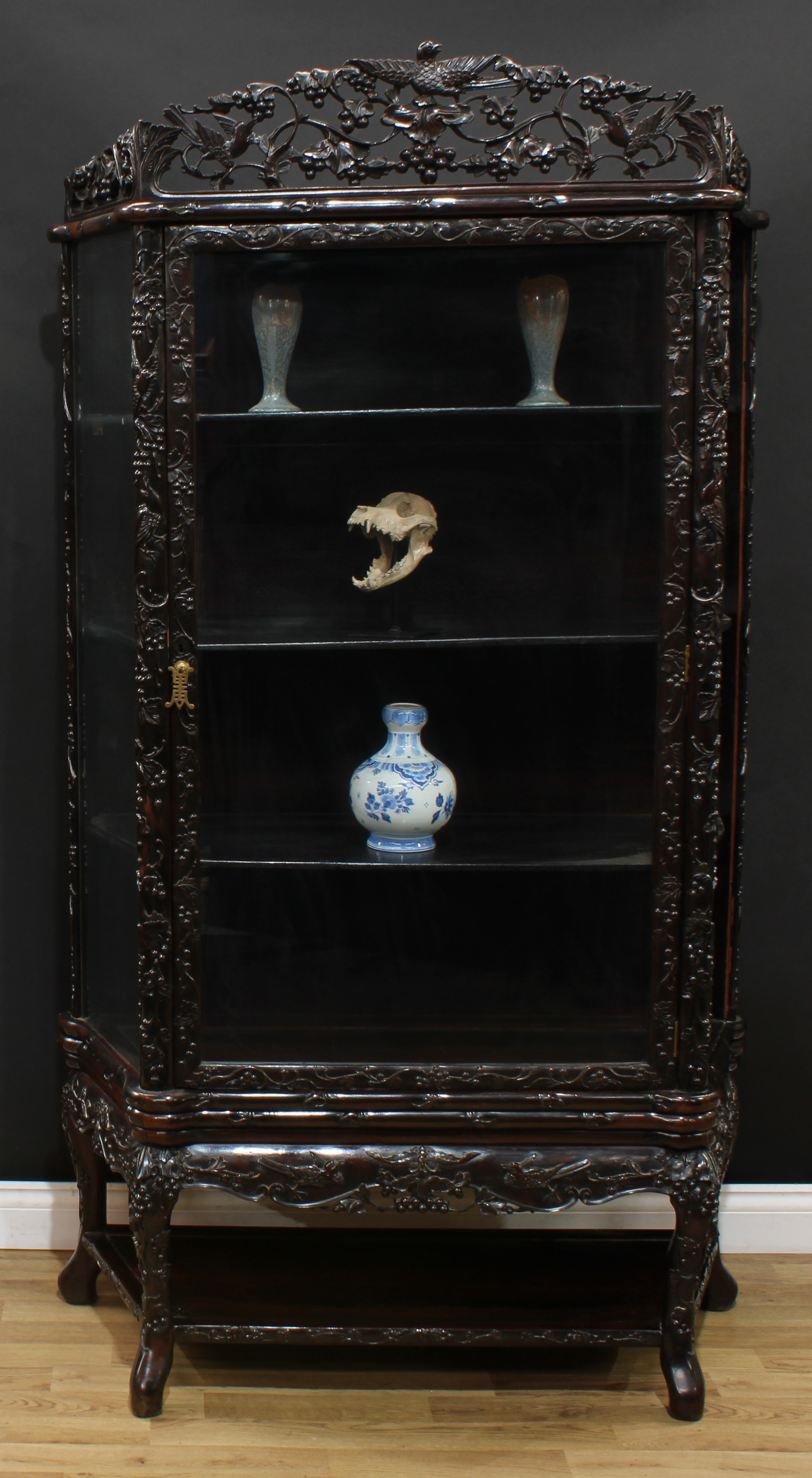 A Chinese hardwood display cabinet, shaped and pierced cresting above a rectangular door, carved throughout with birds and fruiting vine, open undertier, outswept feet, 195cm high, 110.5cm wide, 46cm deep, c.1900
